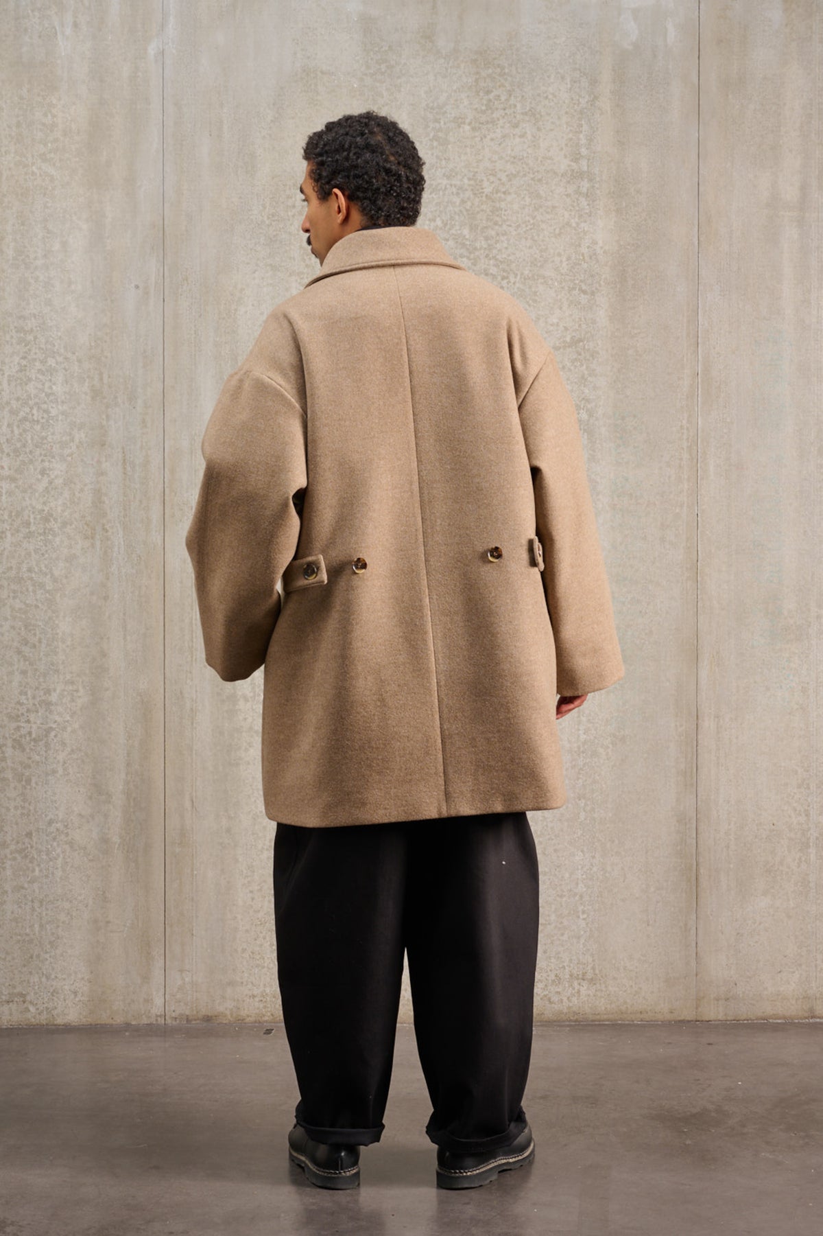 Manteau croisé oversize de la marque Aïdama, modèle Haomi en laine et cachemire beige. Porté fermé par un mannequin homme et vu de dos.