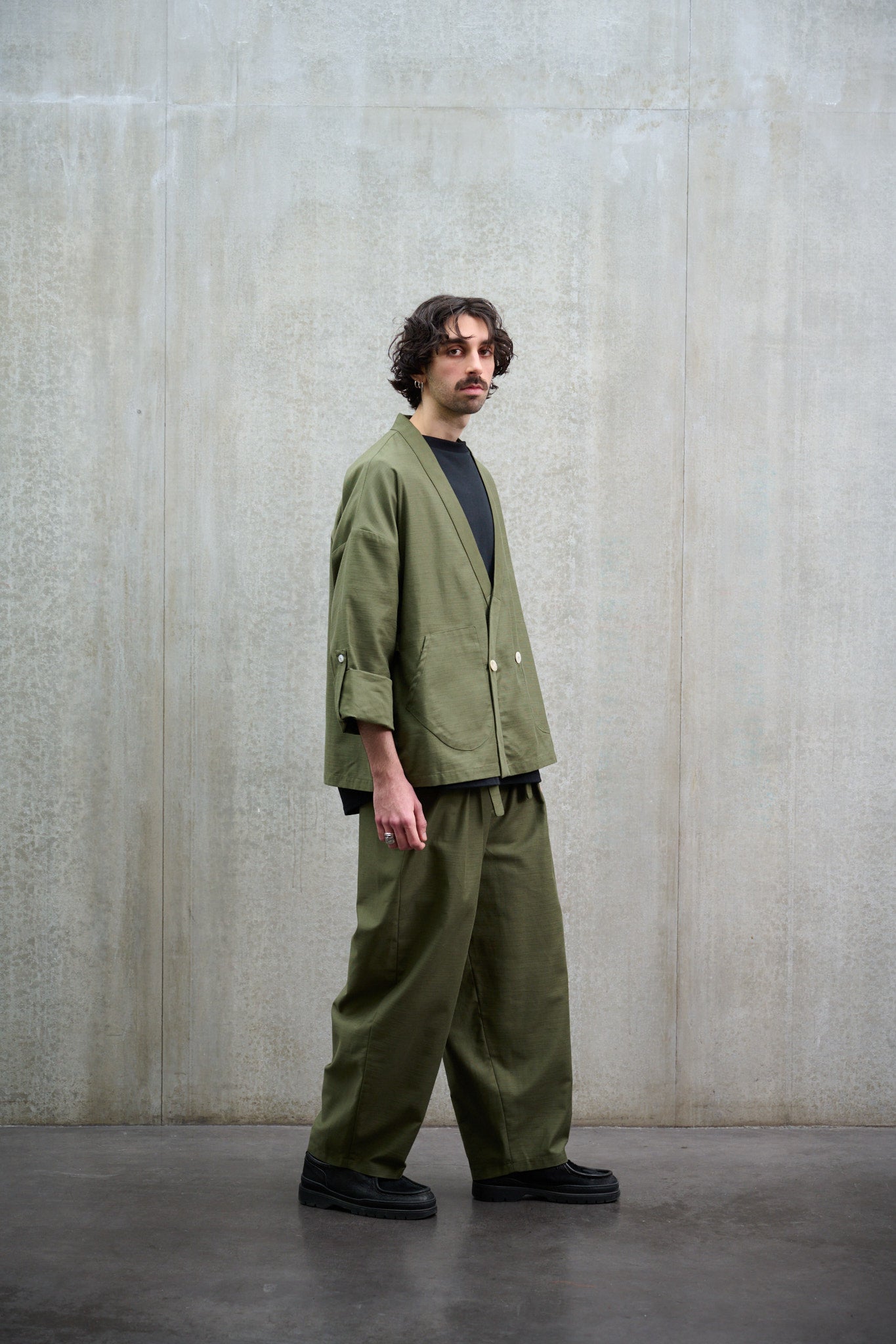 Pantalon circulaire Aïdama, coupe ballon avec ceinture ajustable en coton texturé vert. Porté par un mannequin homme et vu de profil.