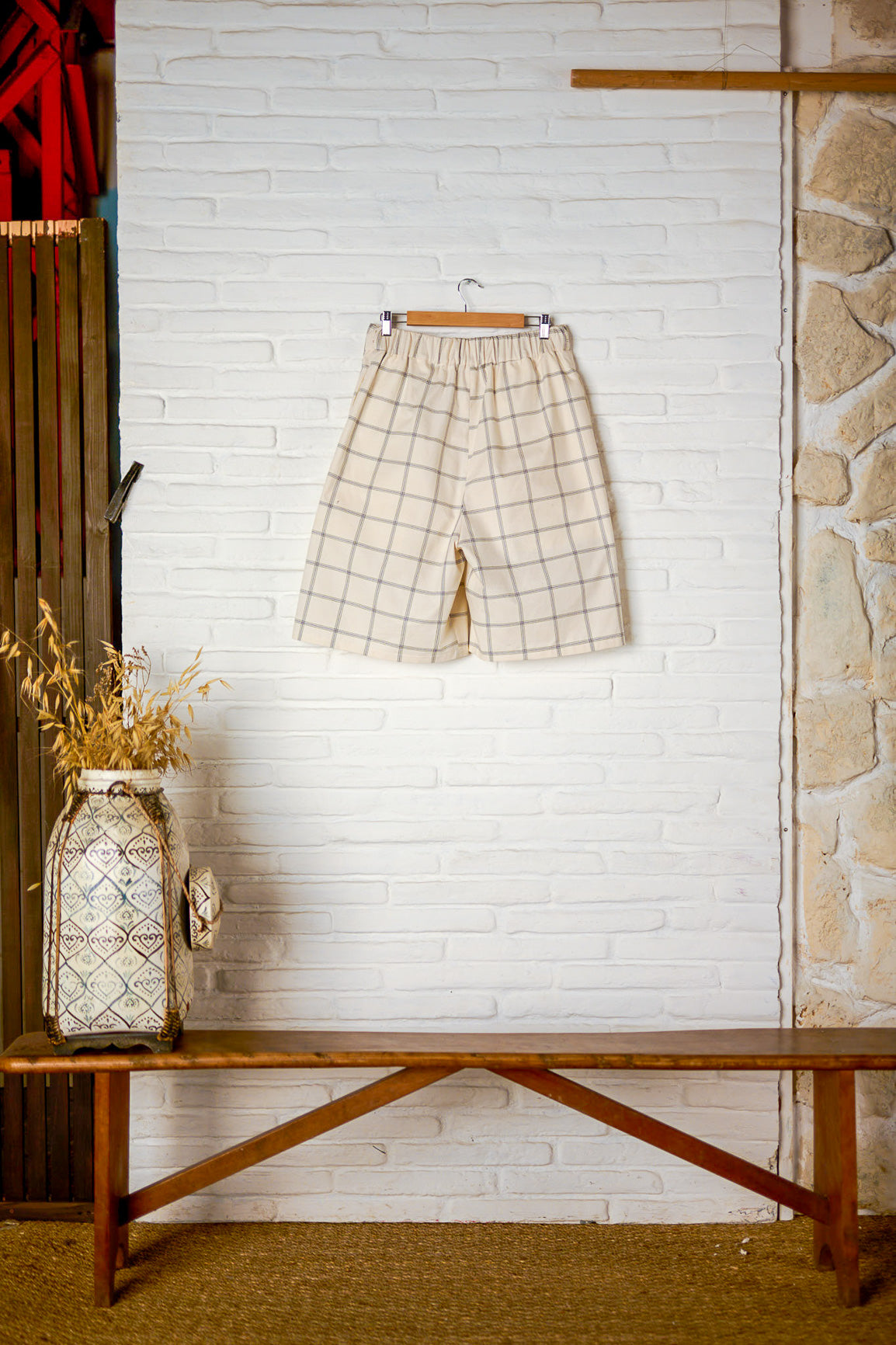 Short ballon de la marque Aïdama en coton crème à carreaux avec ceinture ajustable. Vu sur ceintre et de dos sur fond blanc.