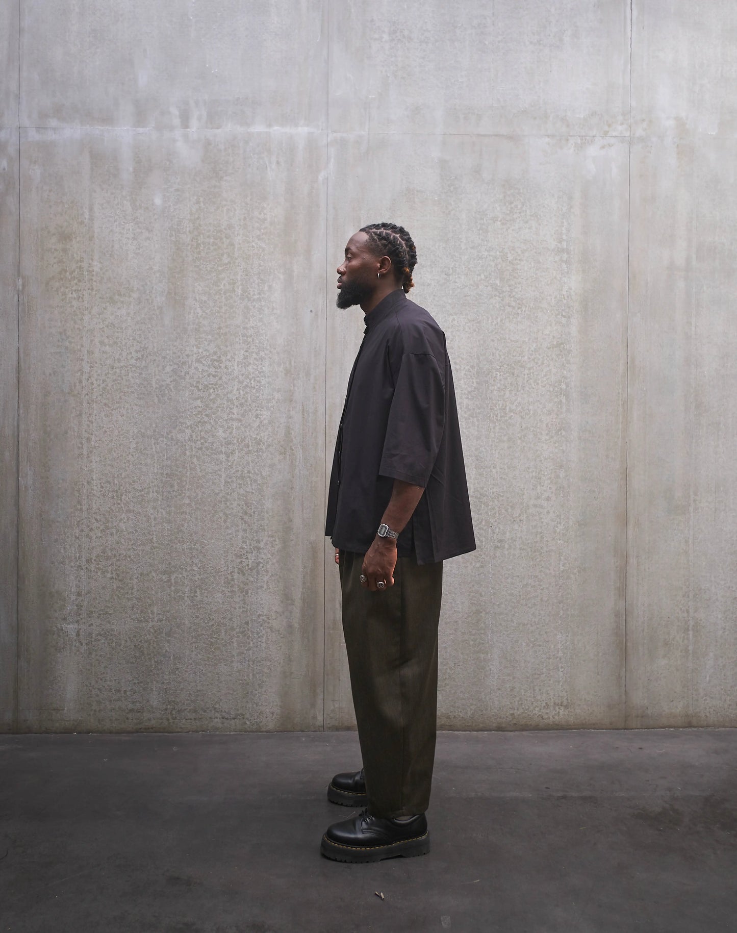 Chemise oversize à col officier de la marque Aïdama, modèle Kita, coupe boxy en popeline de coton noire. Portée par un mannequin homme et vue de profil.