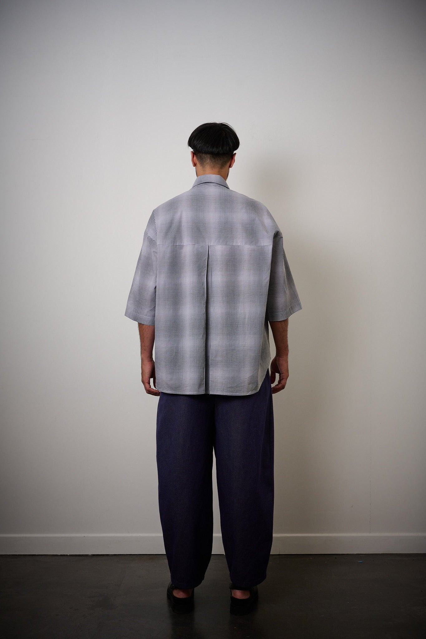 Chemise oversize à manches courtes et col club de la marque Aïdama, modèle Marui en popeline de coton à carreaux flous bleu-gris. Portée par un mannequin homme et vue de dos.