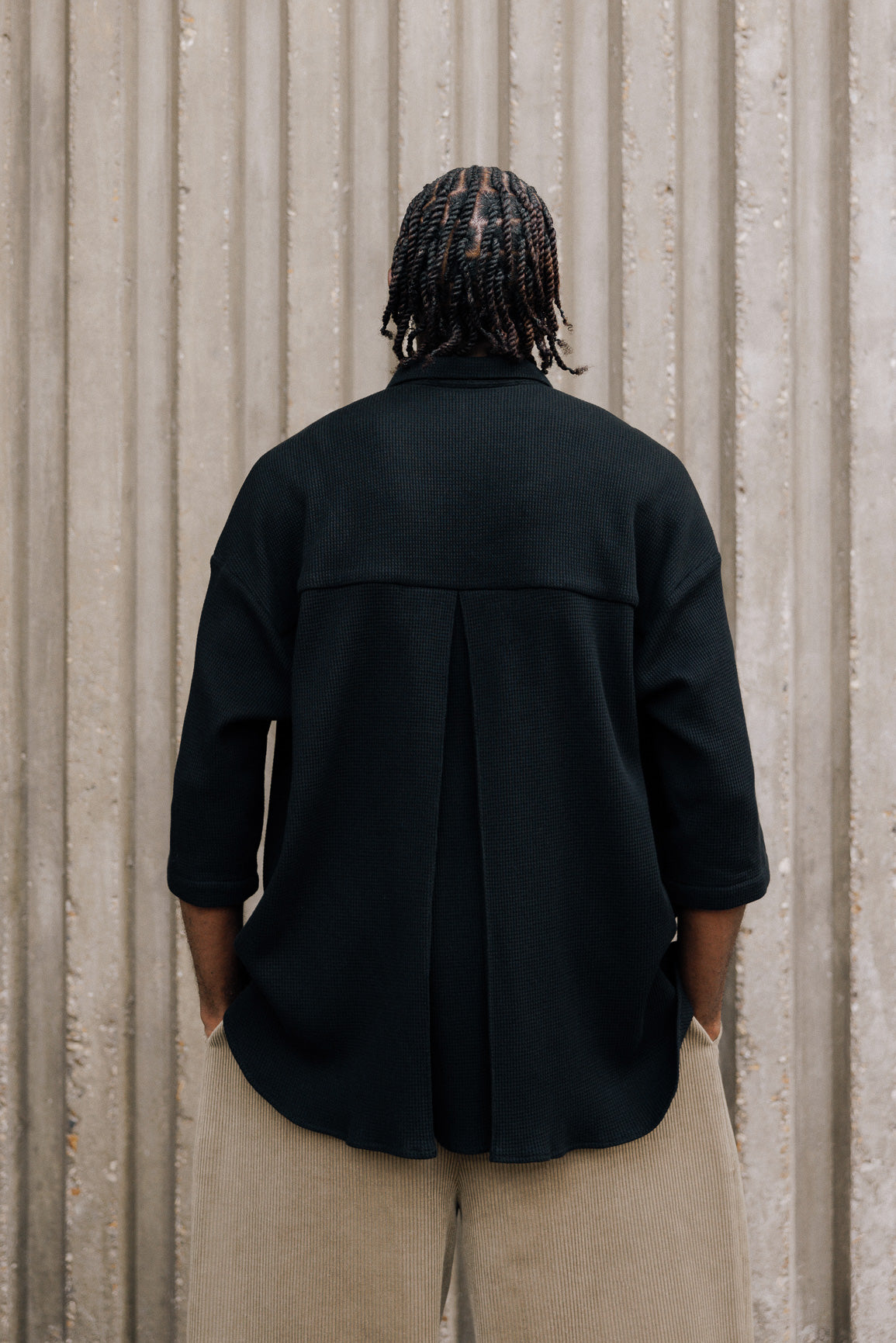 Chemise oversize à manches courtes et col club de la marque Aïdama, modèle Marui en coton nid d’abeille noir. Portée par un mannequin homme et vue de dos.