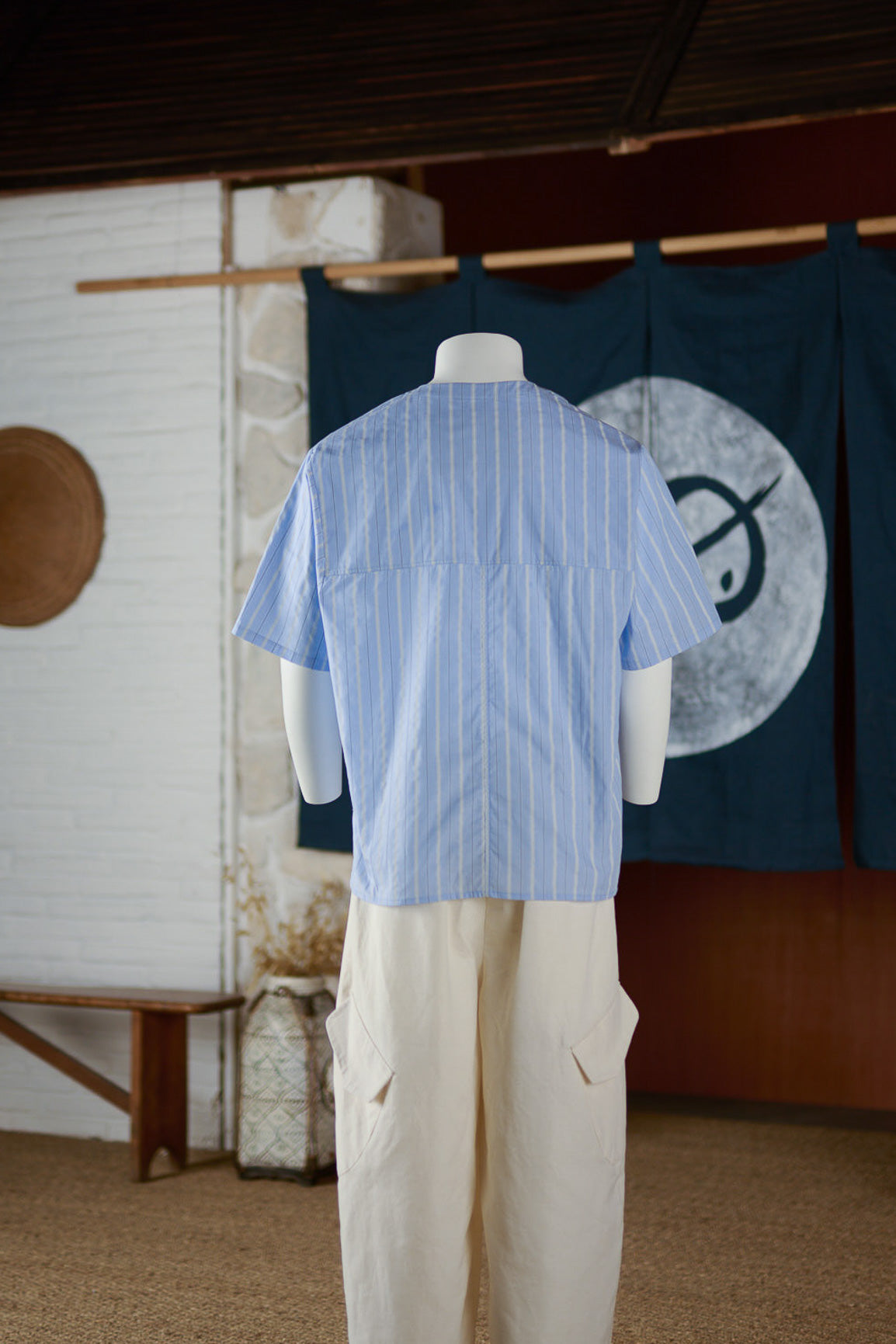 Chemise popover oversize à col tunisien et poche poitrine de la marque Aïdama, en coton bleu à rayures. Vue de dos sur mannequin.