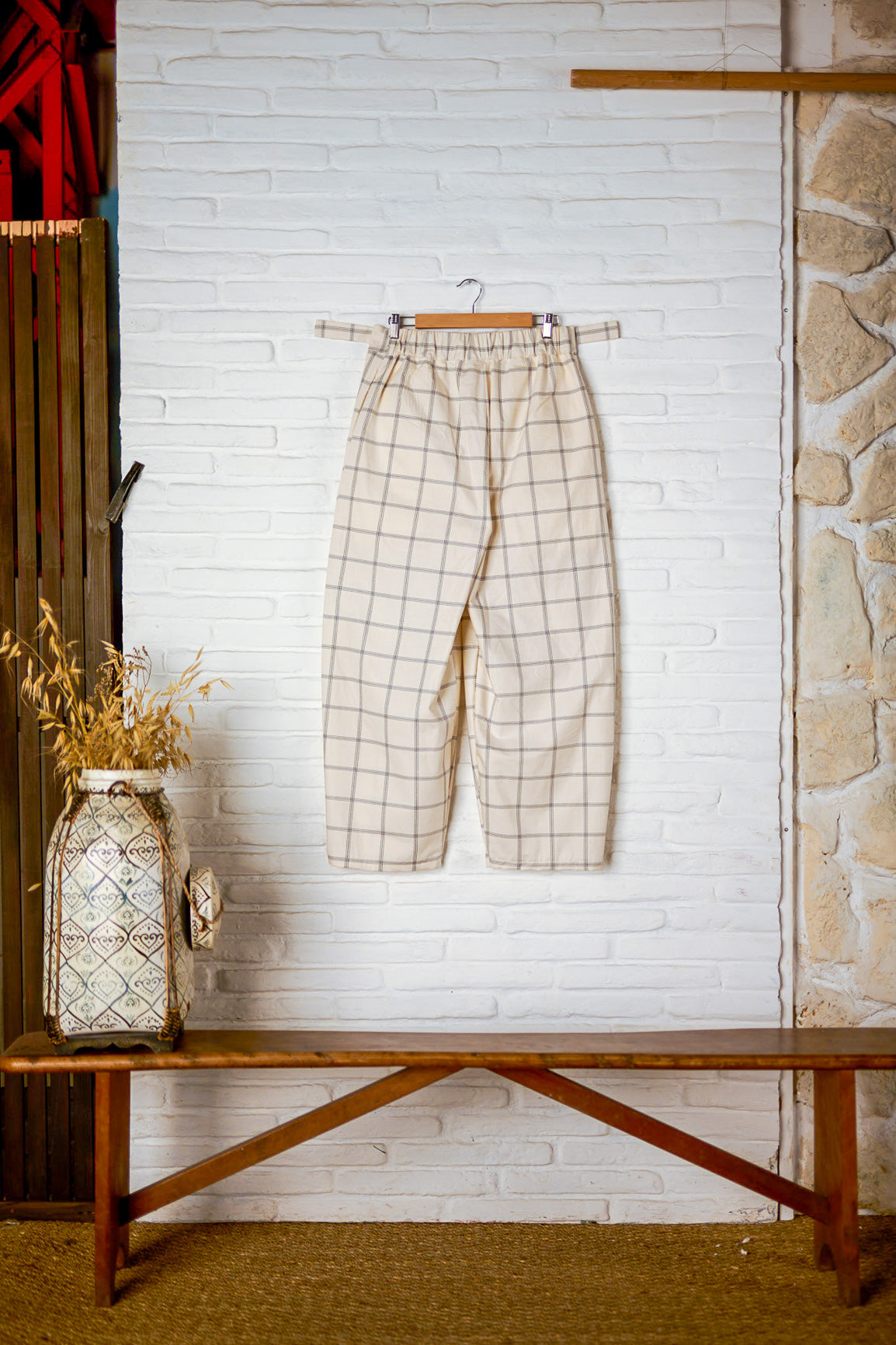 Pantalon circulaire de la marque Aïdama, coupe ballon en coton crème à carreaux. Vu sur ceintre et fond blanc de dos.