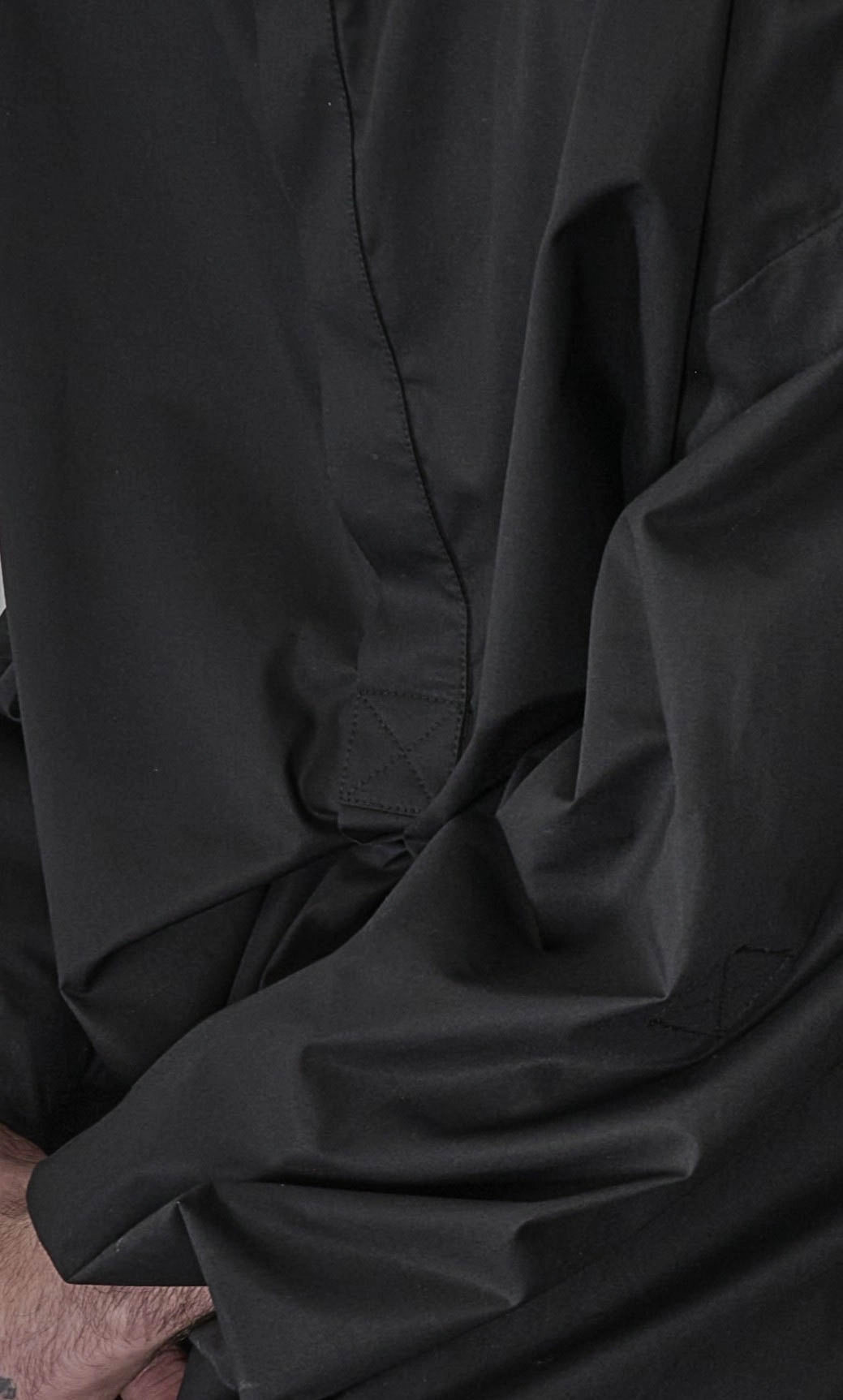 Chemise oversize à manche longue et col rond Aïdama modèle Ao en popeline de coton noir. Portée par un mannequin homme et vue zoomée sur le tissu et la boutonnière.