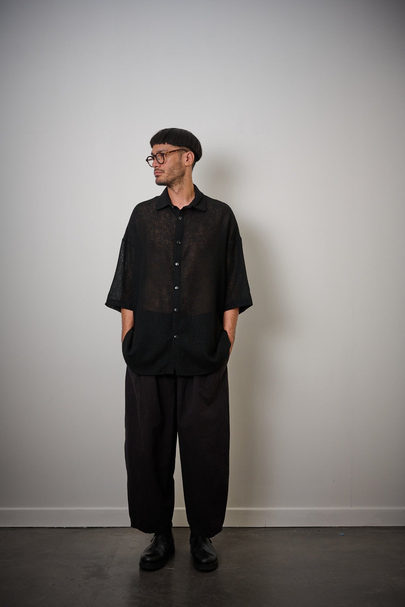 Chemise oversize à col club de la marque Aïdama en crêpe de laine noire légèrement transparente. Portée fermée par un mannequin homme et vue de face. 