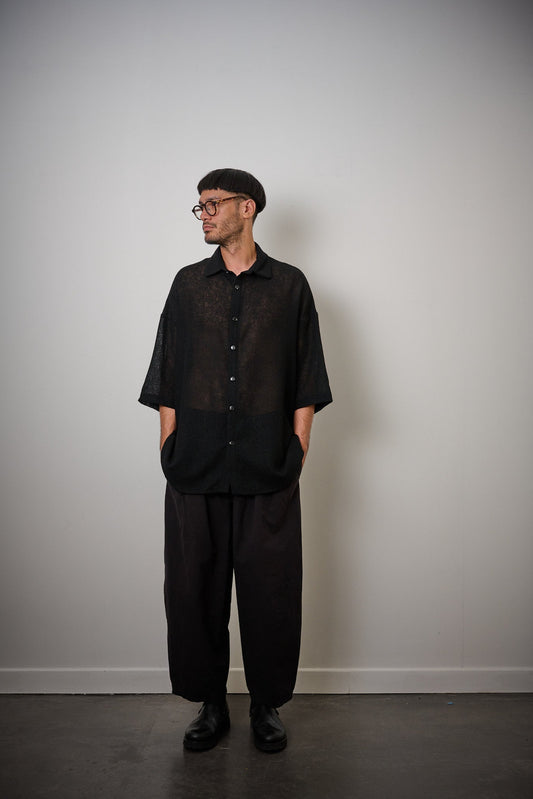 Chemise oversize à col club de la marque Aïdama en crêpe de laine noire légèrement transparente. Portée fermée par un mannequin homme et vue de face. 