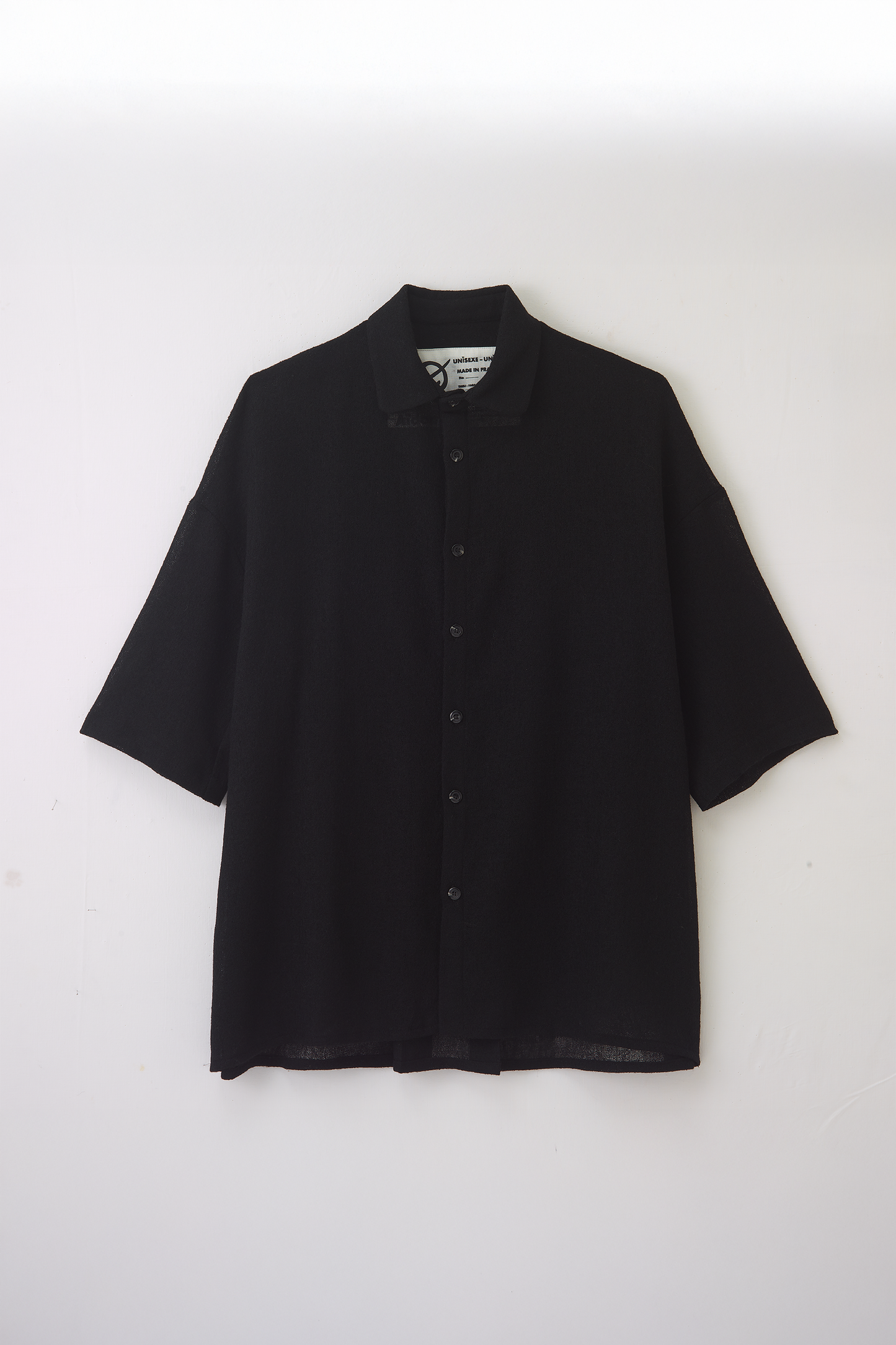 Chemise oversize à col club de la marque Aïdama en crêpe de laine noire légèrement transparente. Vue à plat sur fond blanc.