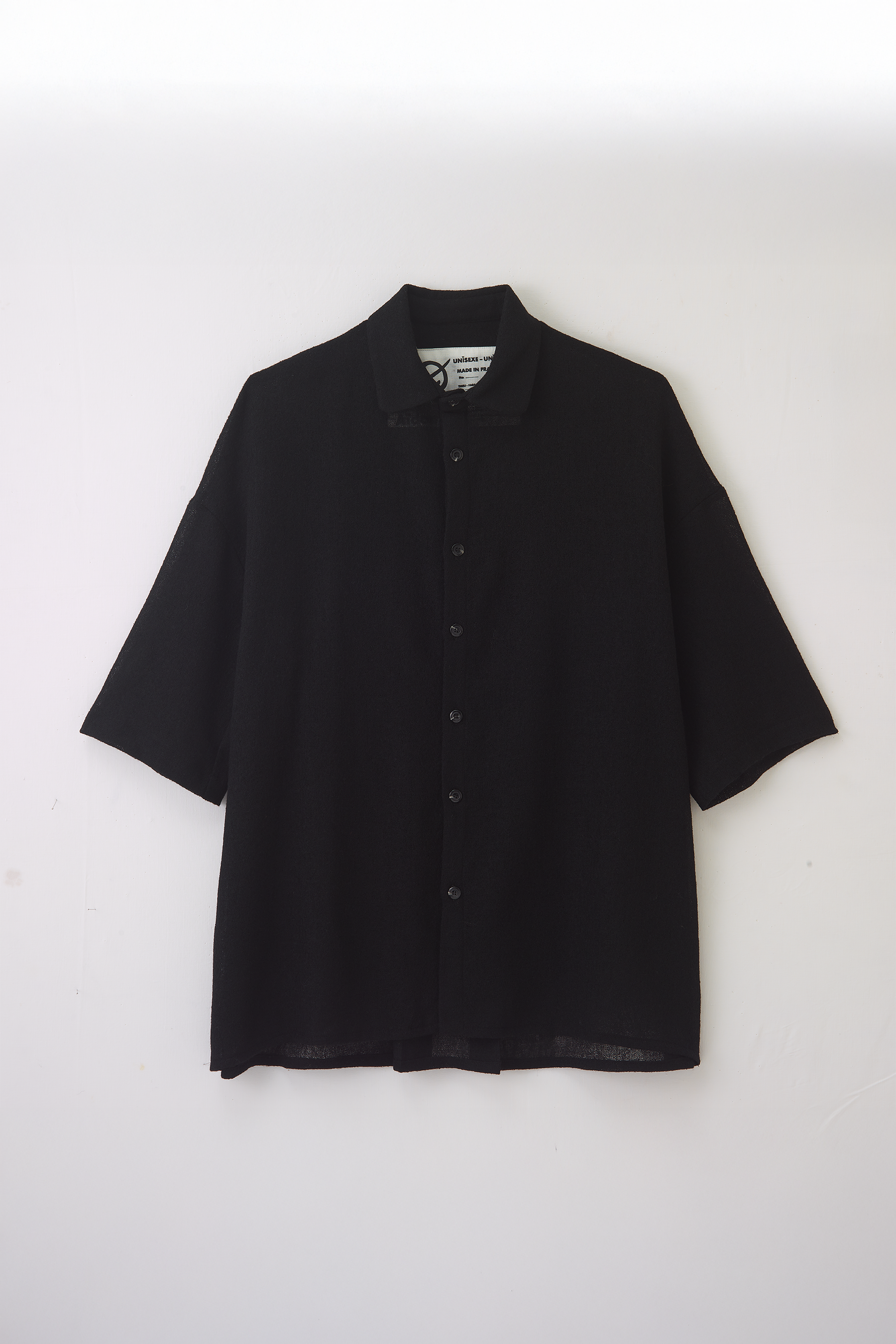 Chemise oversize à col club de la marque Aïdama en crêpe de laine noire légèrement transparente. Vue à plat sur fond blanc.
