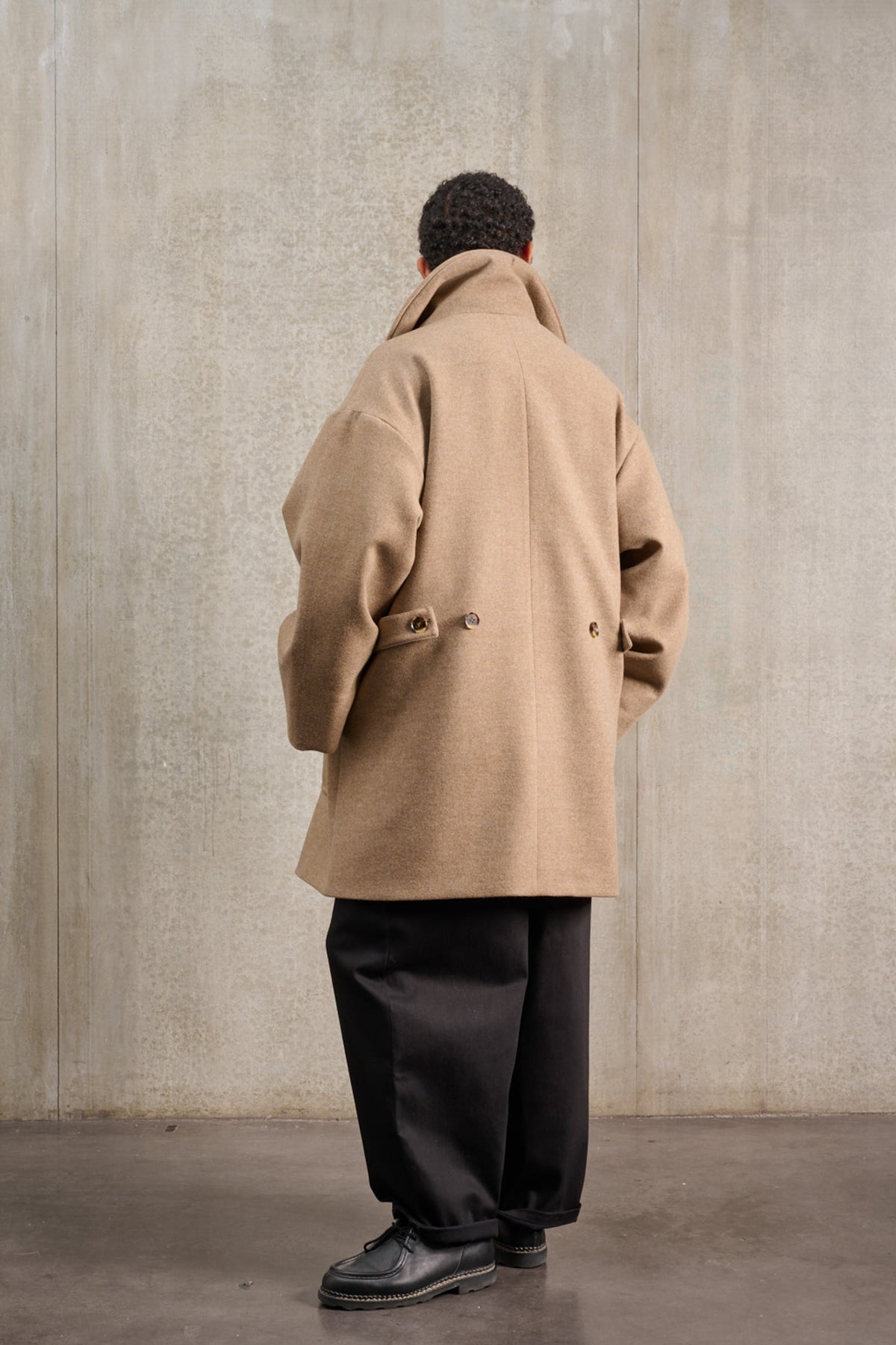 Manteau croisé oversize de la marque Aïdama, modèle Haomi en laine et cachemire beige. Porté fermé par un mannequin homme et vu de dos.