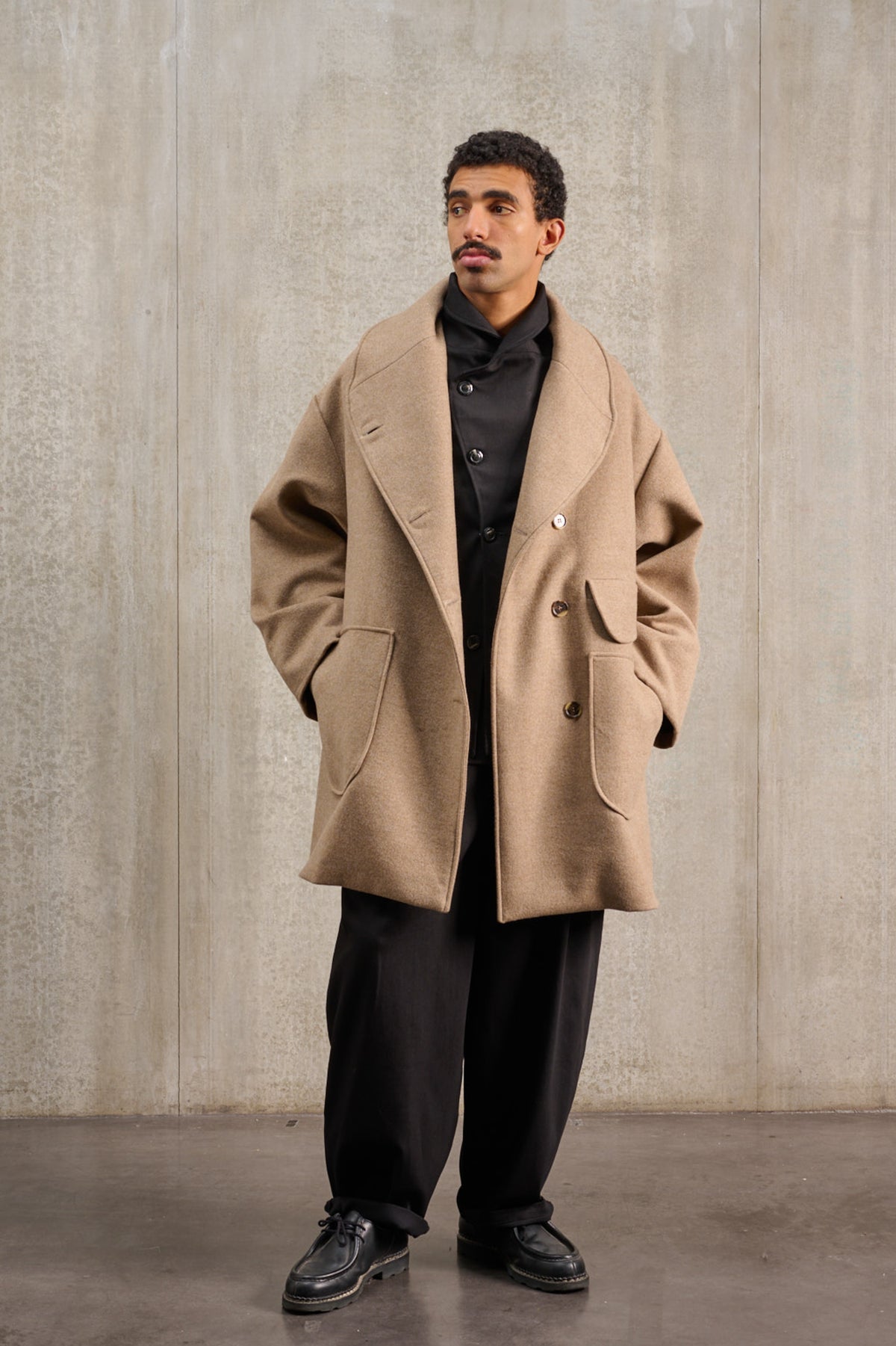 Manteau croisé oversize de la marque Aïdama, modèle Haomi en laine et cachemire beige. Porté ouvert par un mannequin homme et vu de face.
