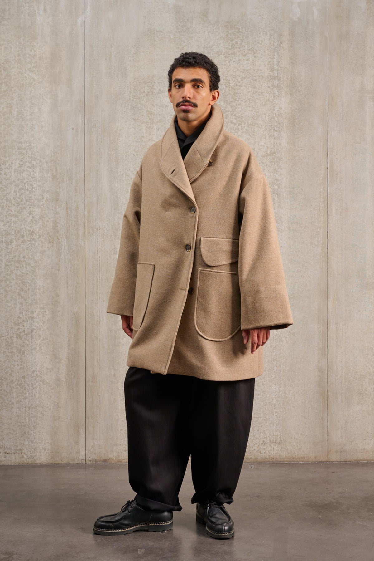 Manteau croisé oversize de la marque Aïdama, modèle Haomi en laine et cachemire beige. Porté fermé par un mannequin homme et vu de trois quarts.