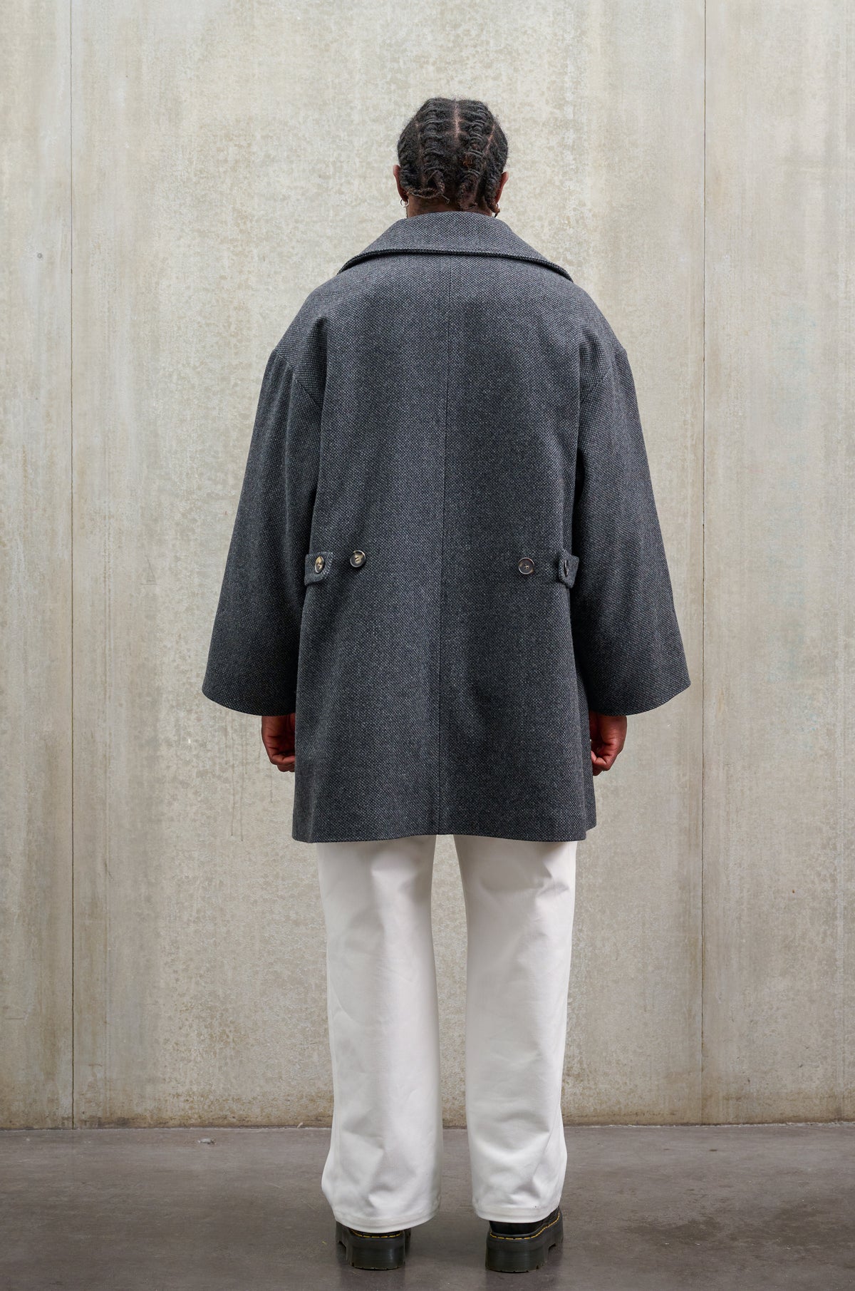 Manteau croisé oversize de la marque Aïdama, modèle Haomi en laine à micro motif damier gris et noir. Porté ouvert par un mannequin homme et vu de dos.