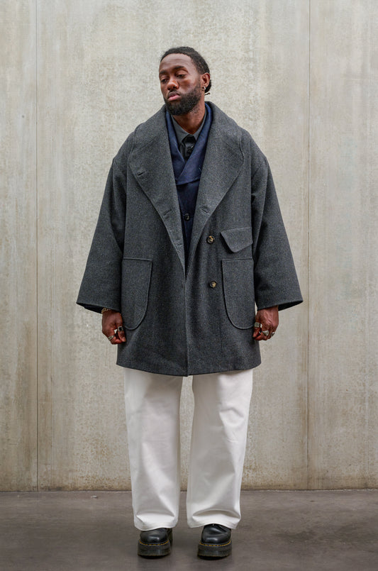 Manteau croisé oversize de la marque Aïdama, modèle Haomi en laine à micro motif damier gris et noir. Porté ouvert par un mannequin homme et vu de face.
