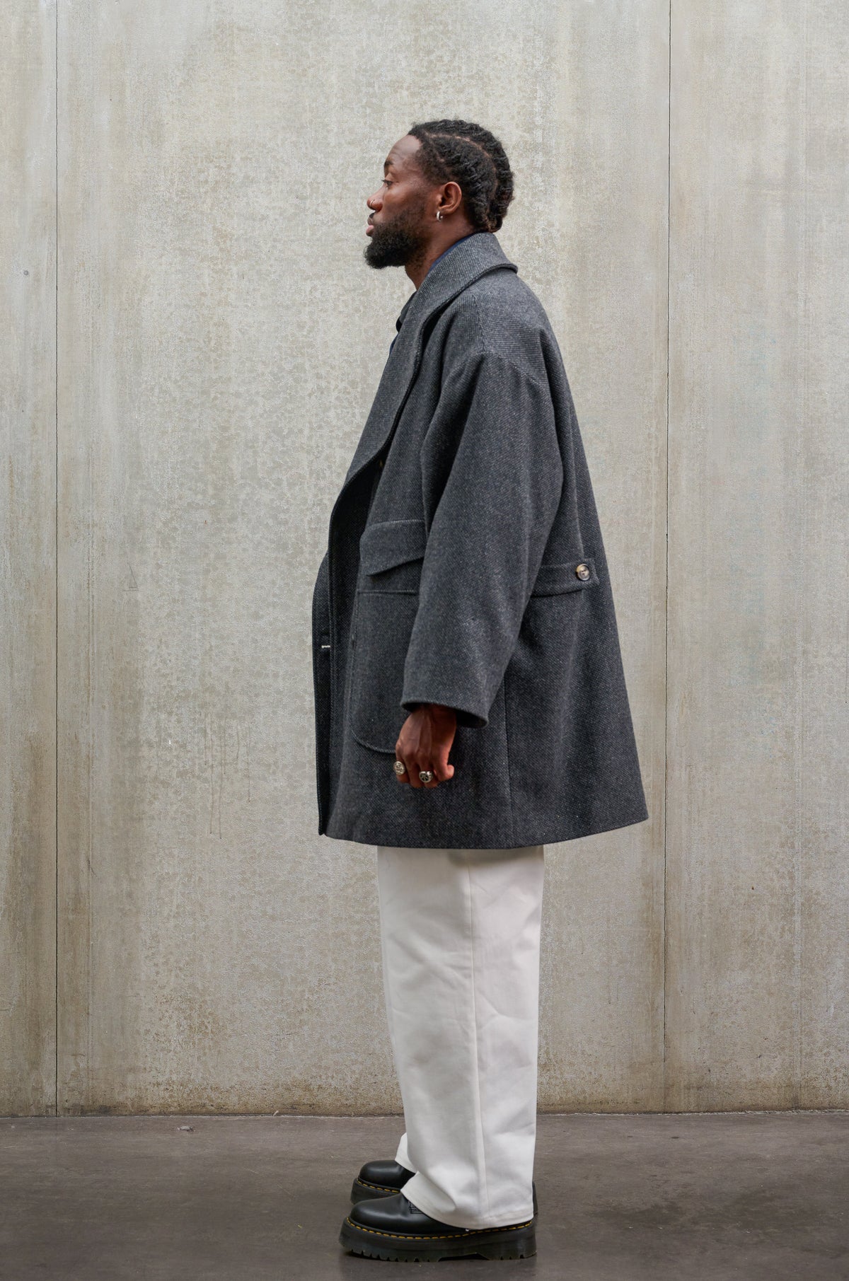 Manteau croisé oversize de la marque Aïdama, modèle Haomi en laine à micro motif damier gris et noir. Porté ouvert par un mannequin homme et vu de profil.