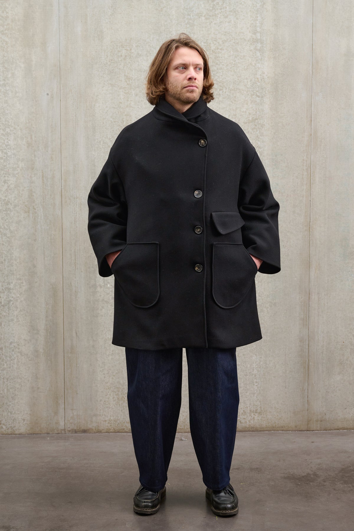 Manteau croisé oversize de la marque Aïdama, modèle Haomi en laine feutrée noire. Porté fermé par un mannequin homme et vu de face.