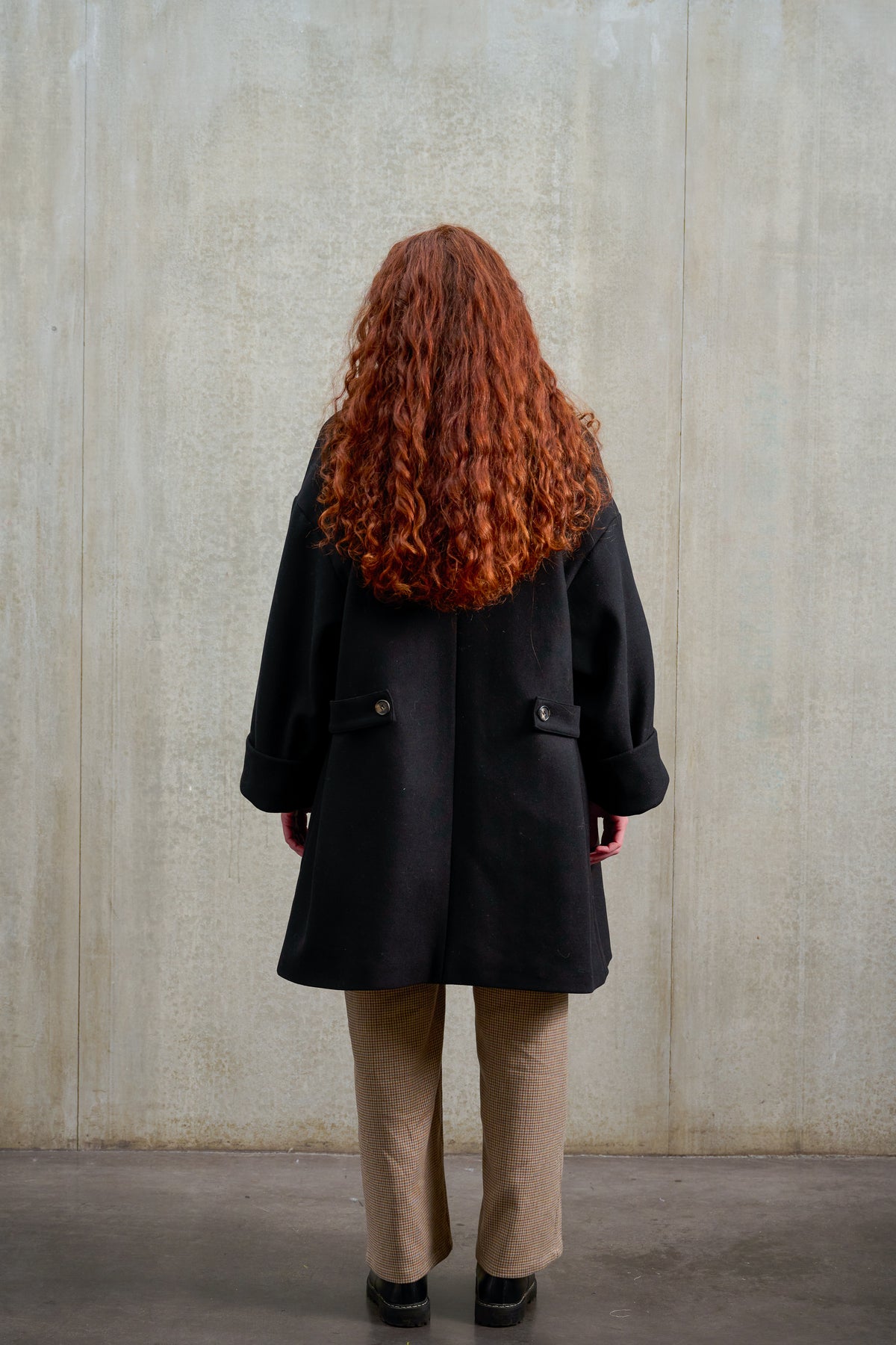 Manteau croisé oversize de la marque Aïdama, modèle Haomi en laine feutrée noire. Porté ouvert par une mannequin femme et vu de dos.