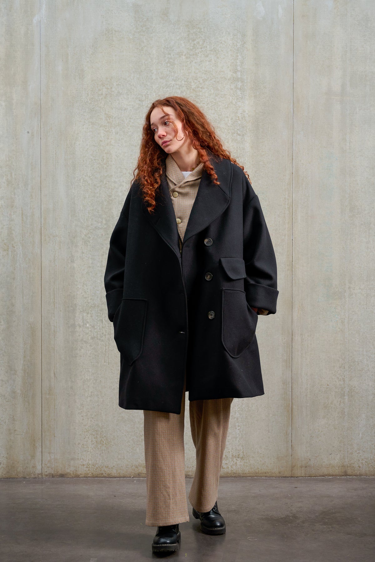 Manteau croisé oversize de la marque Aïdama, modèle Haomi en laine feutrée noire. Porté ouvert par une mannequin femme et vu de face.