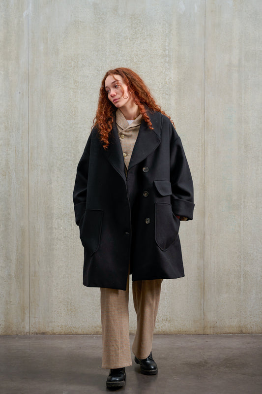 Manteau croisé oversize de la marque Aïdama, modèle Haomi en laine feutrée noire. Porté ouvert par une mannequin femme et vu de face.