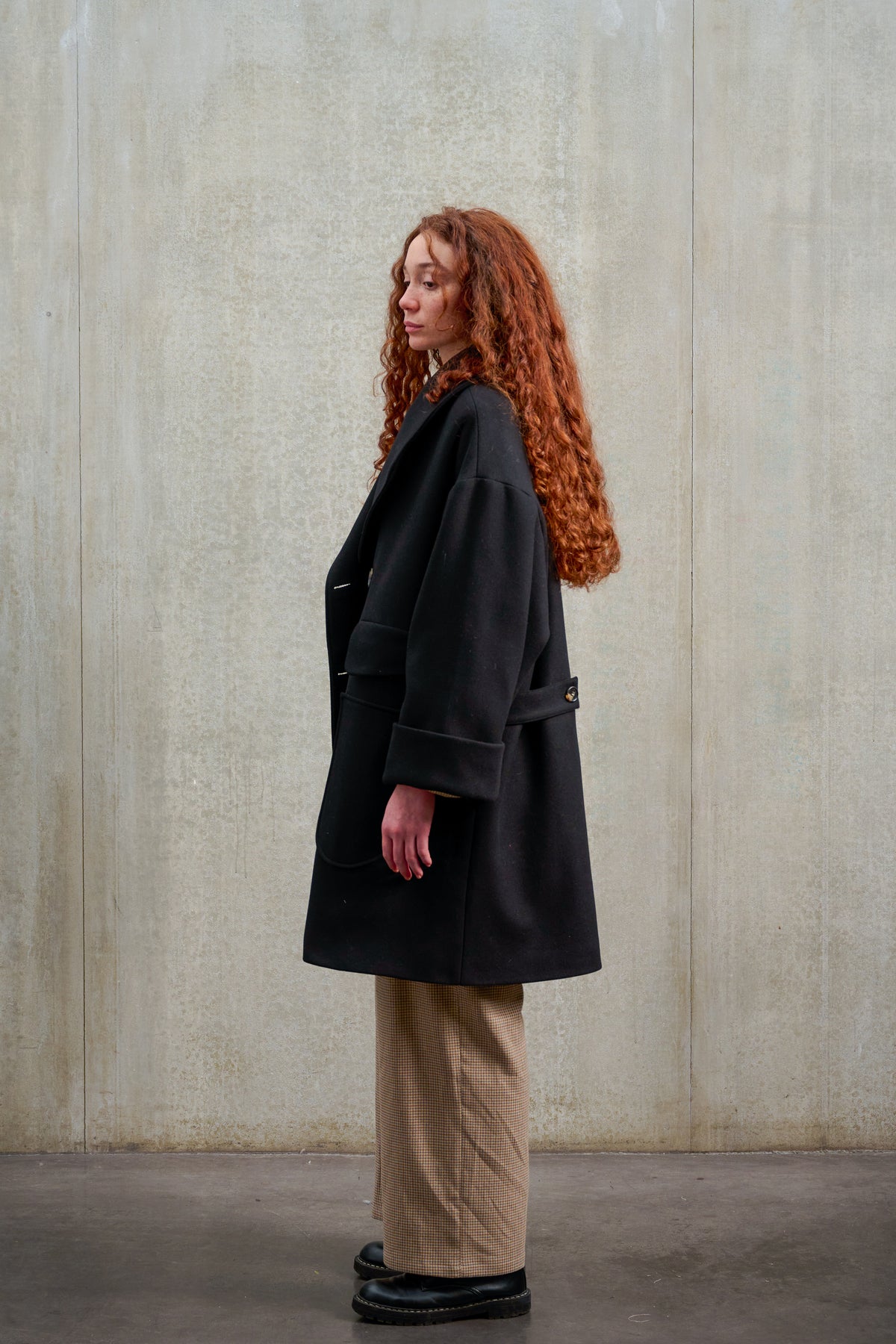 Manteau croisé oversize de la marque Aïdama, modèle Haomi en laine feutrée noire. Porté ouvert par une mannequin femme et vu de profil.