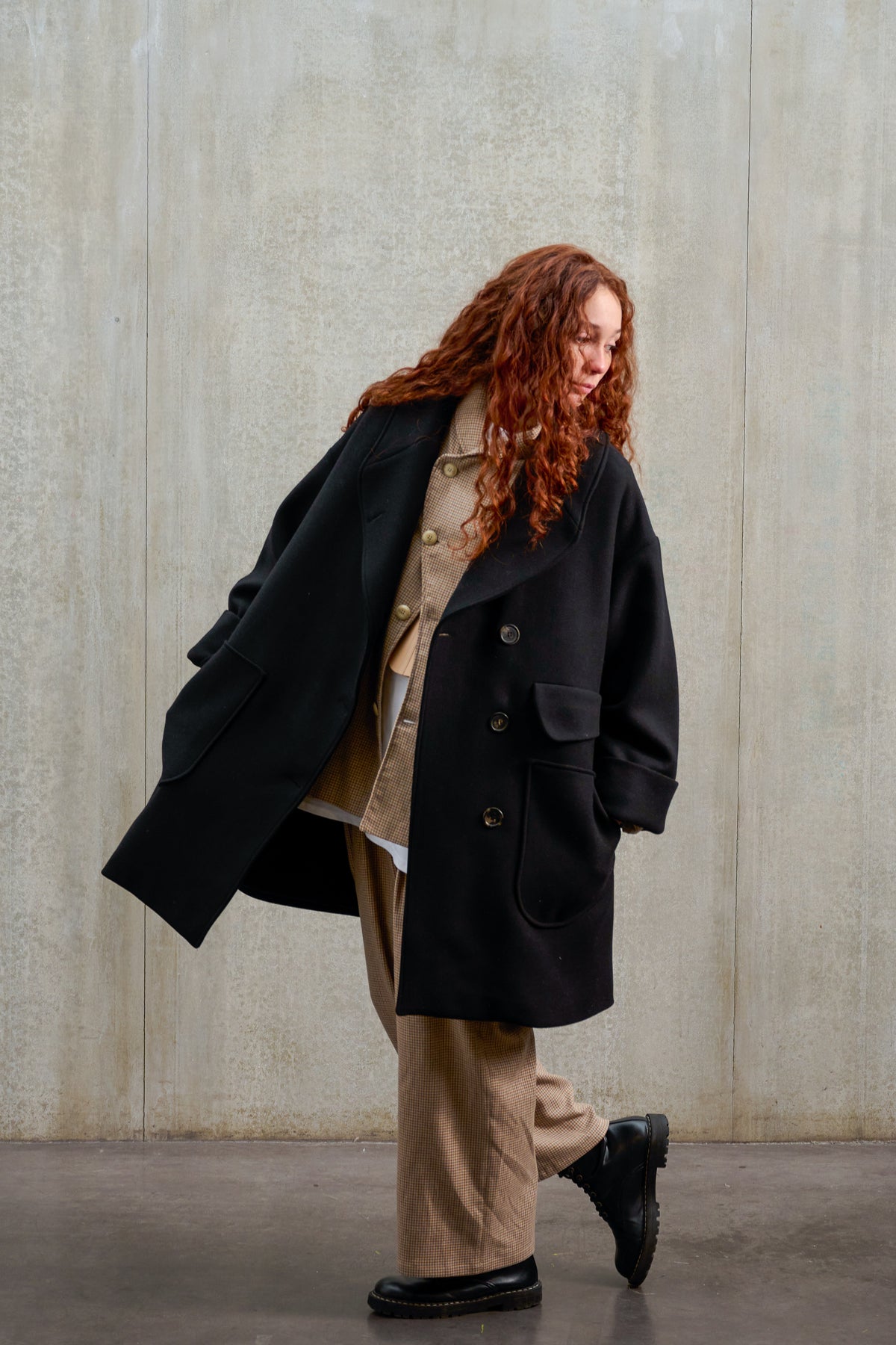Manteau croisé oversize de la marque Aïdama, modèle Haomi en laine feutrée noire. Porté ouvert par une mannequin femme et vu de trois quarts.
