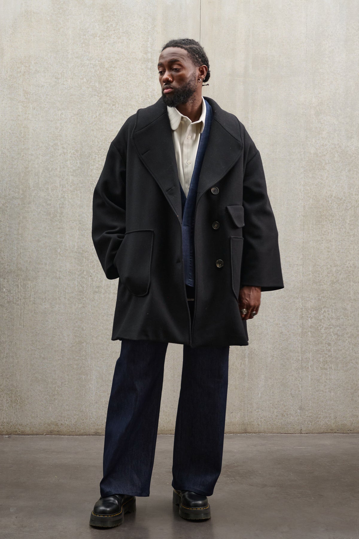 Manteau croisé oversize de la marque Aïdama, modèle Haomi en laine feutrée noire. Porté ouvert par un mannequin homme et vu de face.