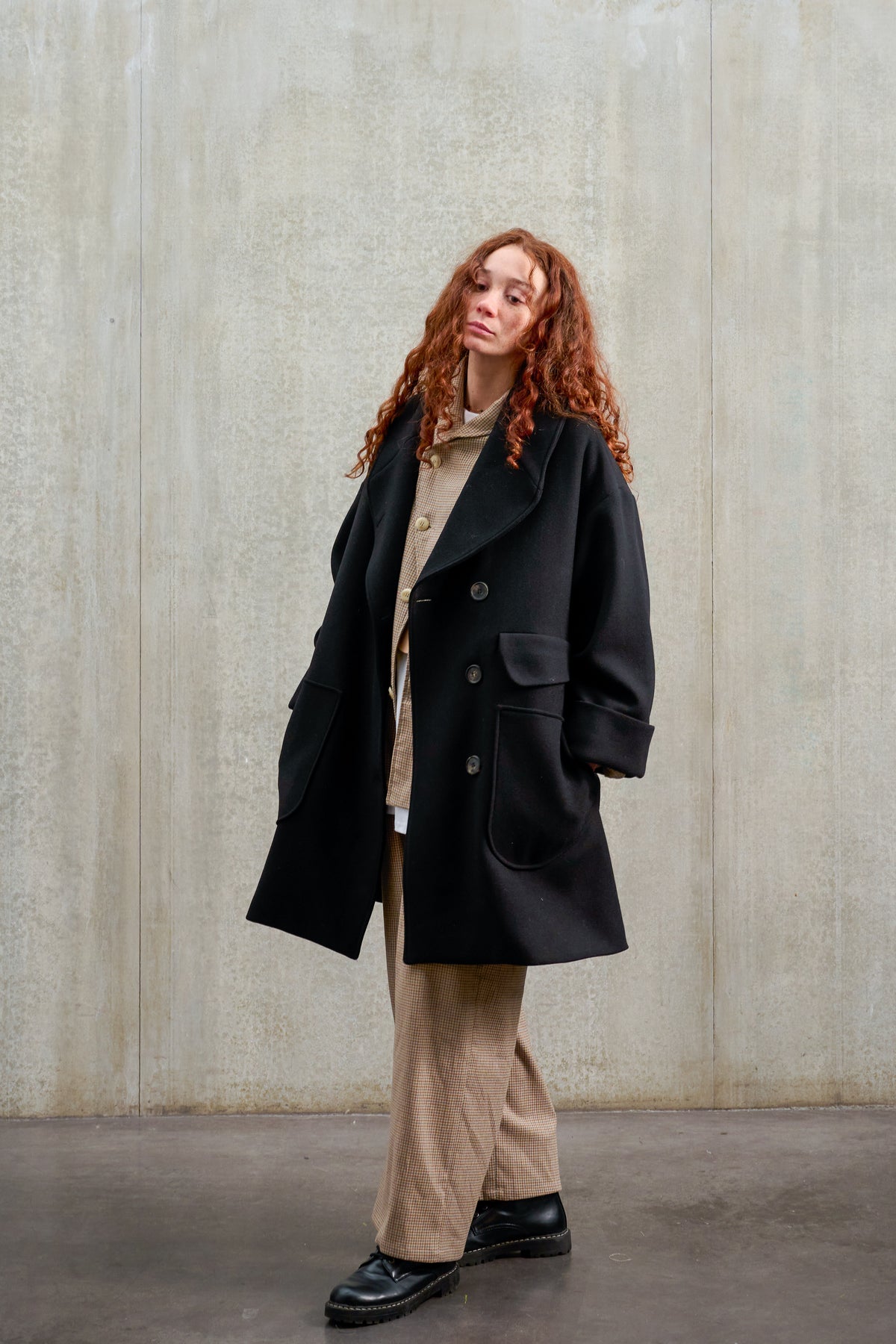 Manteau croisé oversize de la marque Aïdama, modèle Haomi en laine feutrée noire. Porté ouvert par une mannequin femme et vu de trois quarts.
