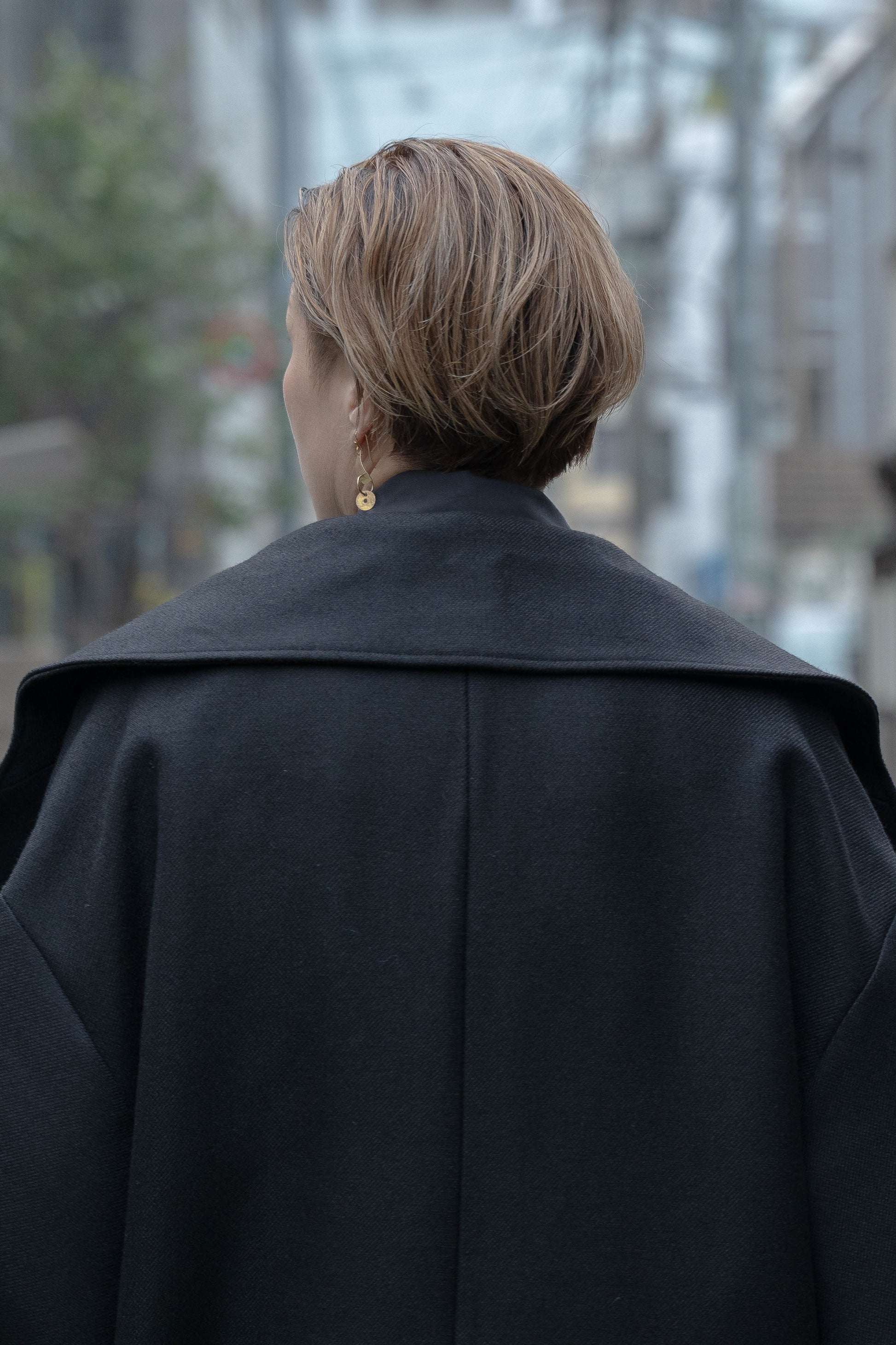 Manteau croisé oversize de la marque Aïdama, modèle Haomi en laine noire. Porté fermé par une mannequin femme et vu zoomé sur le dos en extérieur au Japon.
