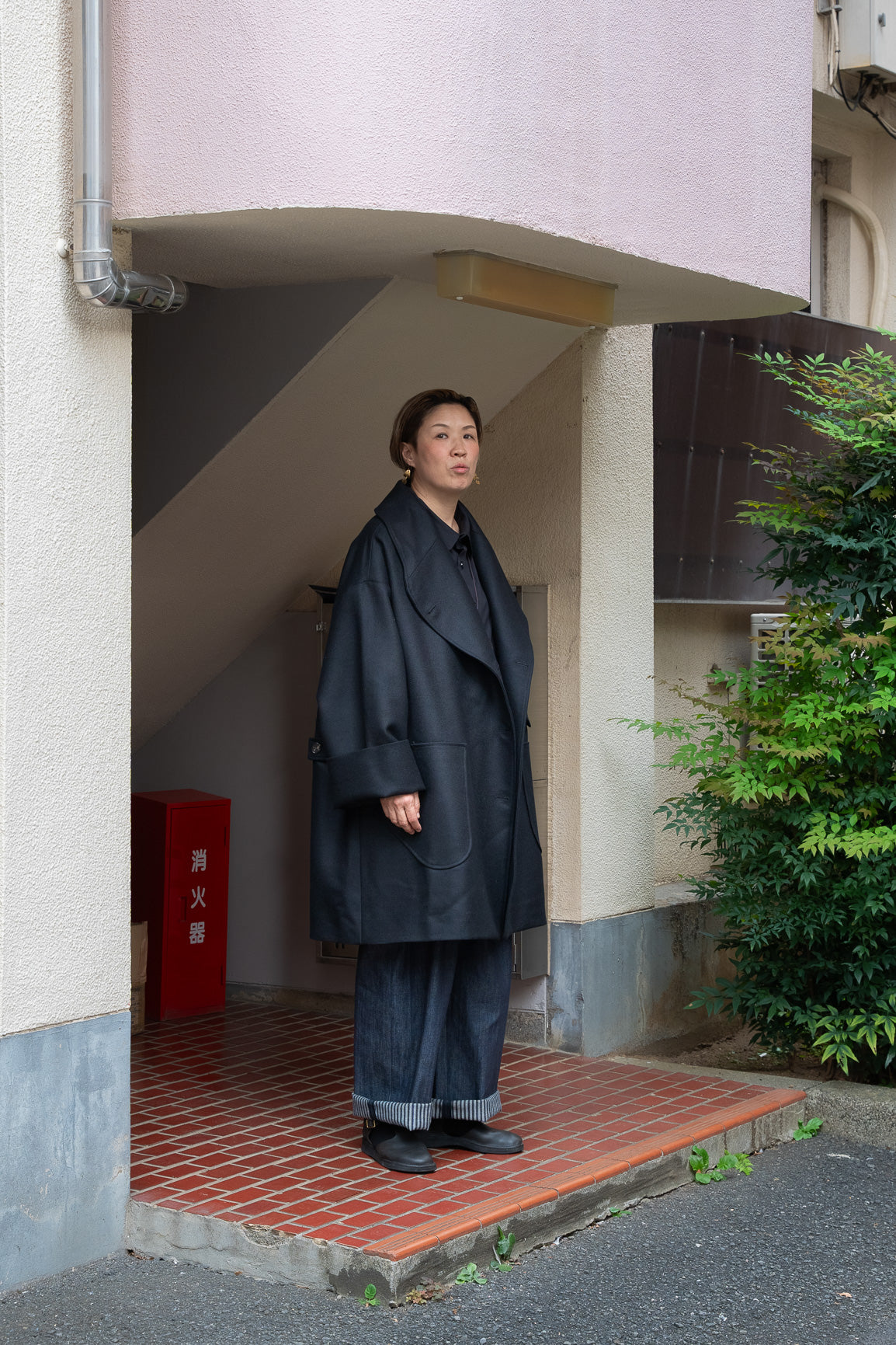 Manteau croisé oversize de la marque Aïdama, modèle Haomi en laine noire. Porté ouvert par une mannequin femme et vu de face en extérieur au Japon.