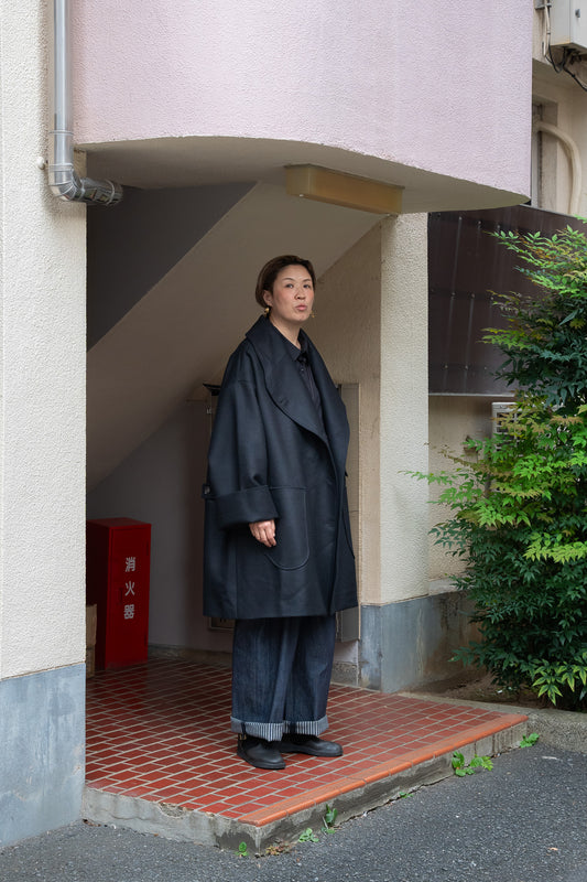 Manteau croisé oversize de la marque Aïdama, modèle Haomi en laine noire. Porté ouvert par une mannequin femme et vu de face en extérieur au Japon.