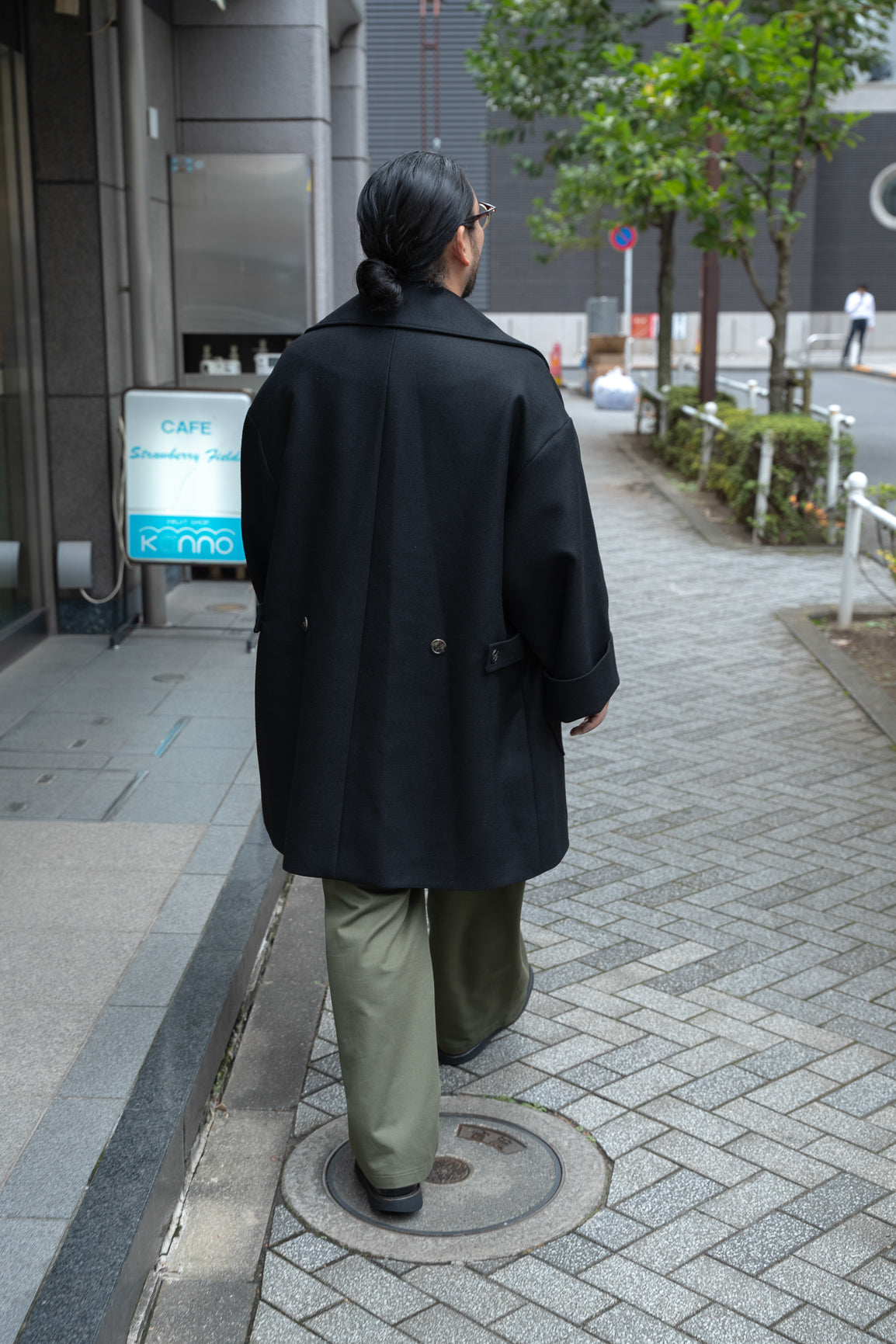 Manteau croisé oversize de la marque Aïdama, modèle Haomi en laine noire. Porté fermé par un mannequin homme et vu de dos en extérieur au Japon.