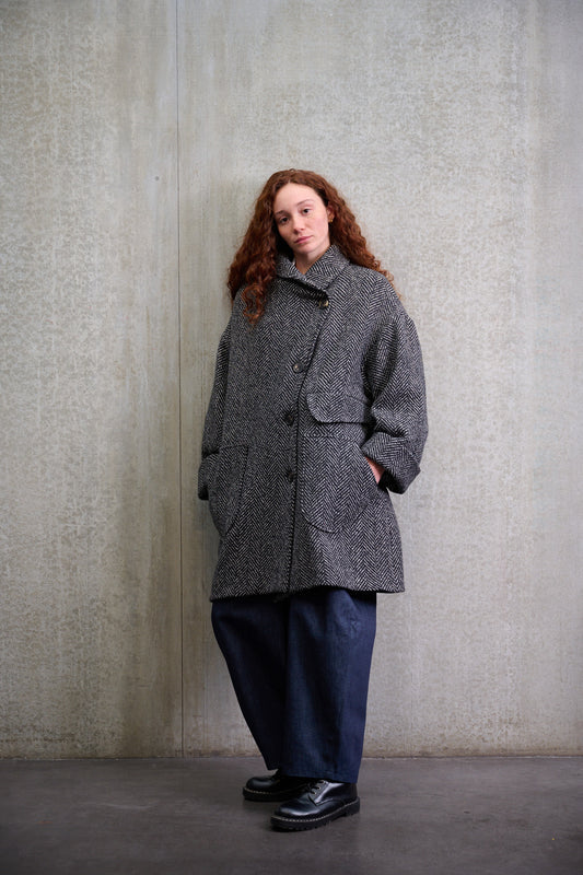 Manteau croisé oversize de la marque Aïdama, modèle Haomi en tweed de laine gris à motif chevrons. Porté fermé par une mannequin femme et vue de face.