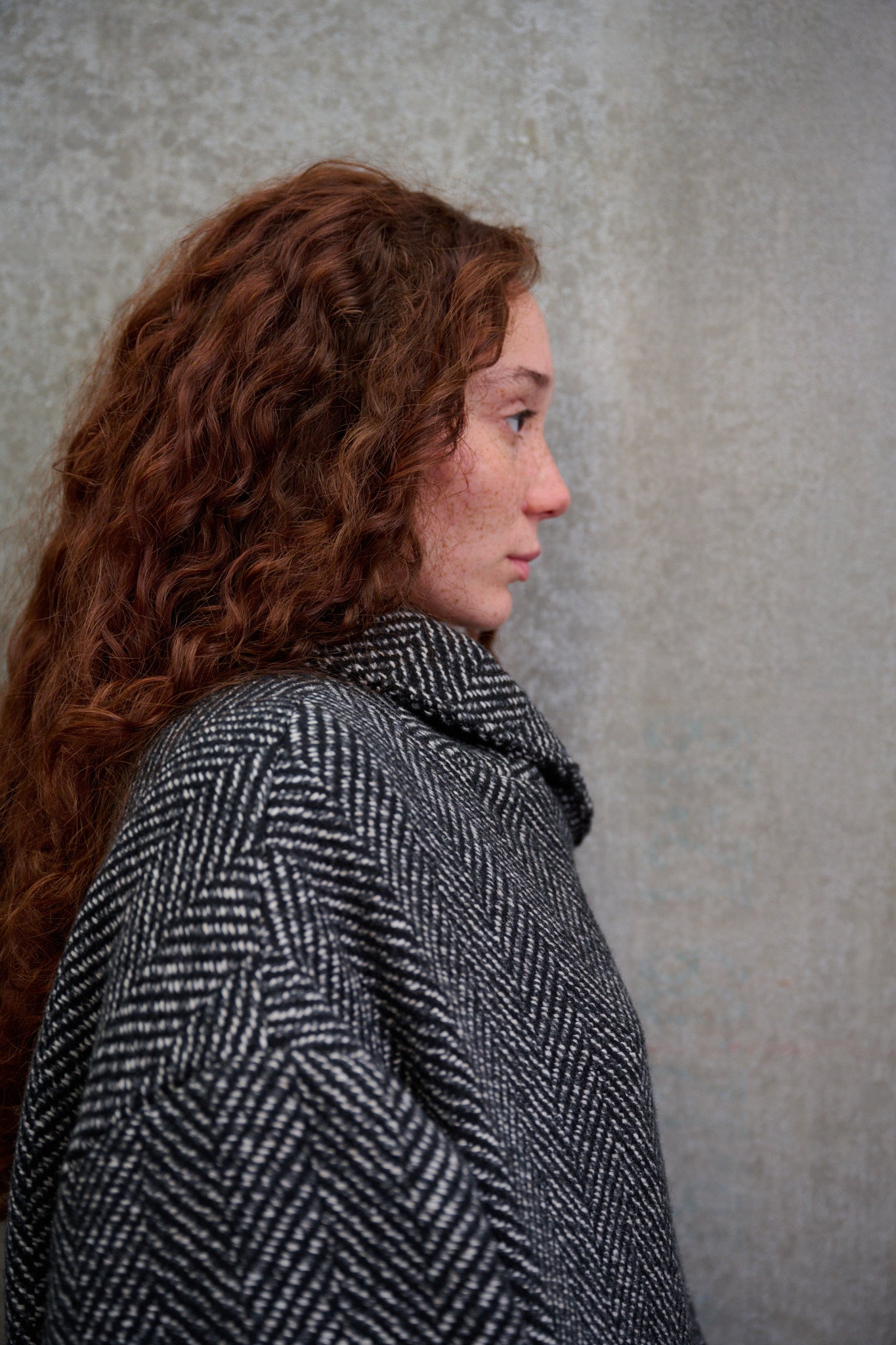Manteau croisé oversize de la marque Aïdama, modèle Haomi en tweed de laine gris à motif chevrons. Porté fermé par une mannequin femme et vue de profil.