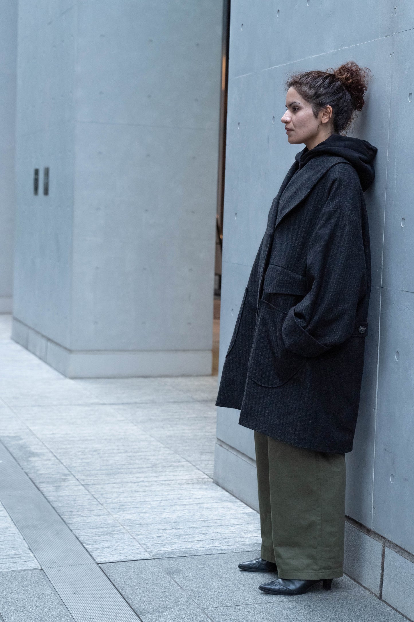 Manteau croisé oversize de la marque Aïdama, modèle Haomi en tweed de laine gris anthracite. Porté fermé par une mannequin femme et vue de profil en extérieur. 