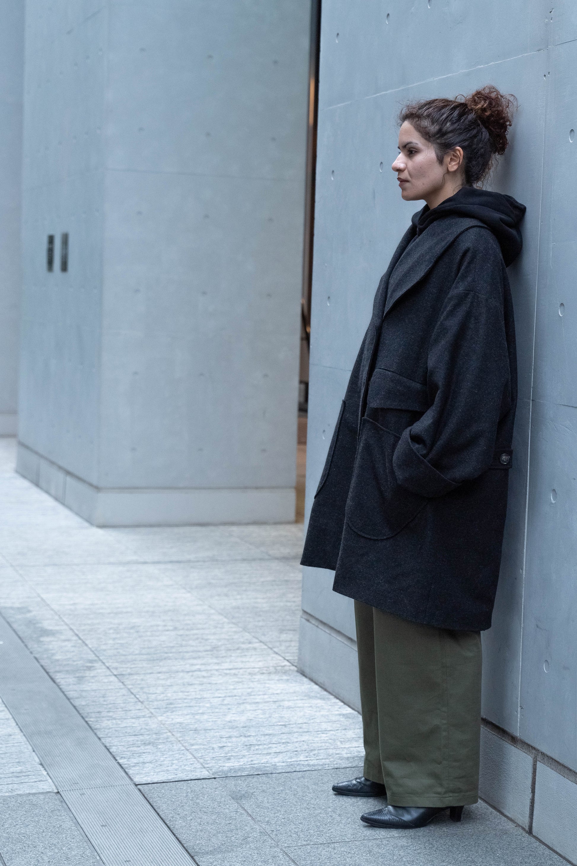Manteau croisé oversize de la marque Aïdama, modèle Haomi en tweed de laine gris anthracite. Porté fermé par une mannequin femme et vue de profil en extérieur. 