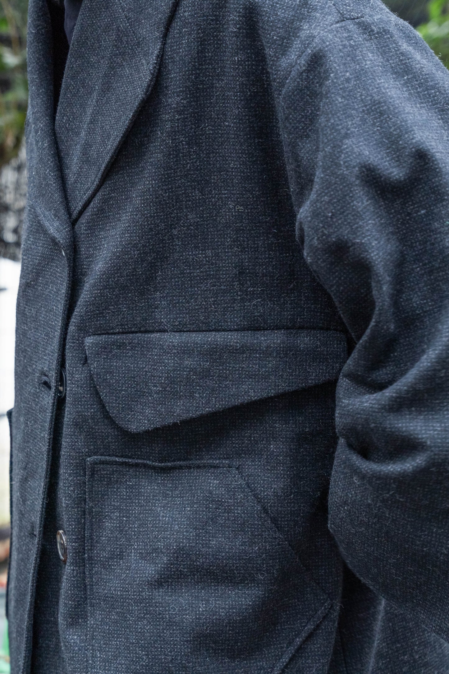 Manteau croisé oversize de la marque Aïdama, modèle Haomi en tweed de laine gris anthracite. Porté fermé par un mannequin homme et vue zoomée sur les poches.
