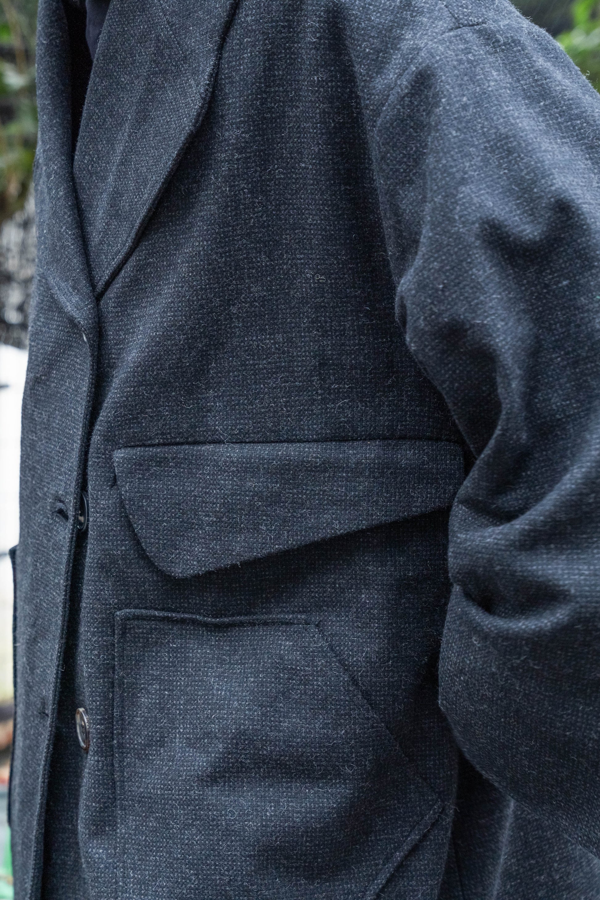Manteau croisé oversize de la marque Aïdama, modèle Haomi en tweed de laine gris anthracite. Porté fermé par un mannequin homme et vue zoomée sur les poches.