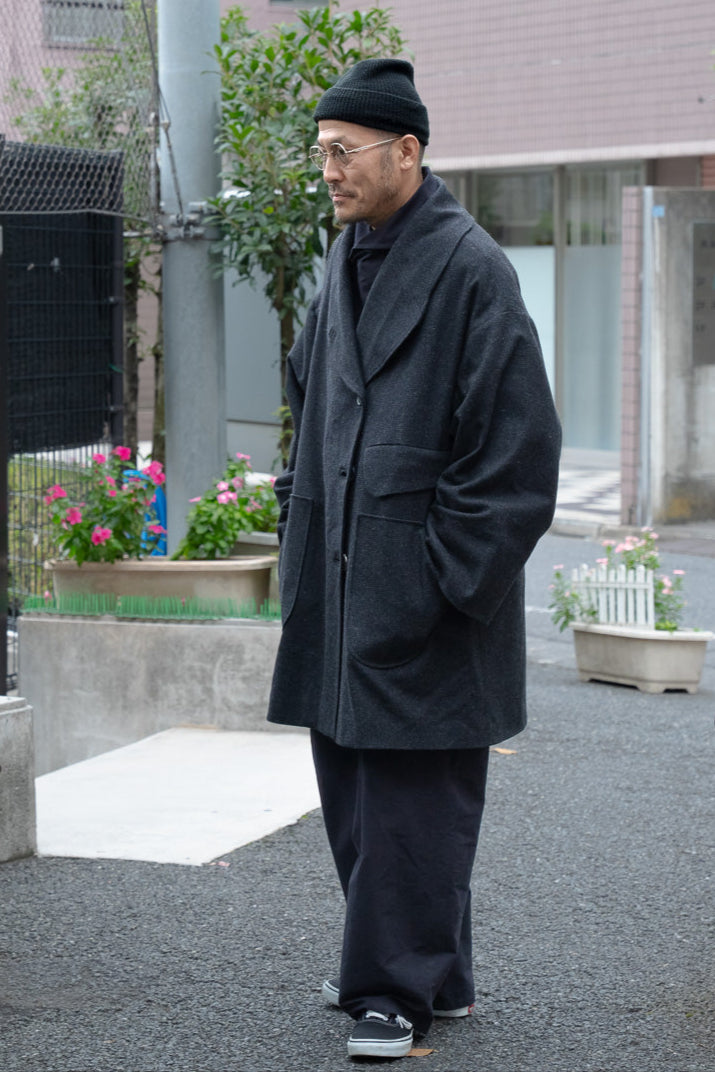 Manteau croisé oversize de la marque Aïdama, modèle Haomi en tweed de laine gris anthracite. Porté fermé par un mannequin homme et vue de trois quarts en extérieur au Japon.