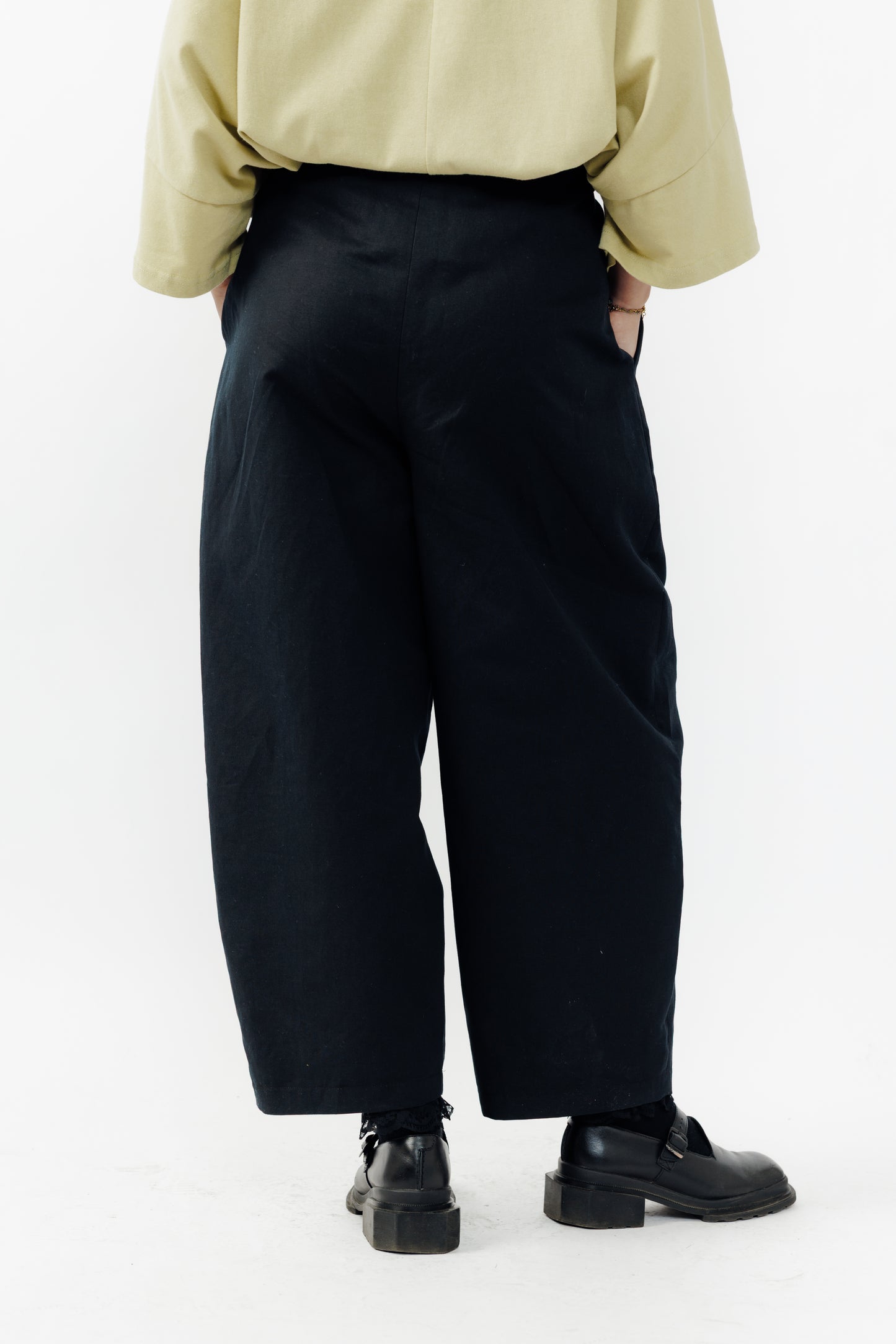 Pantalon circulaire de la marque Aïdama, coupe ballon en coton et lin noir avec ceinture ajustable. Porté par une mannequin femme et vu de dos.