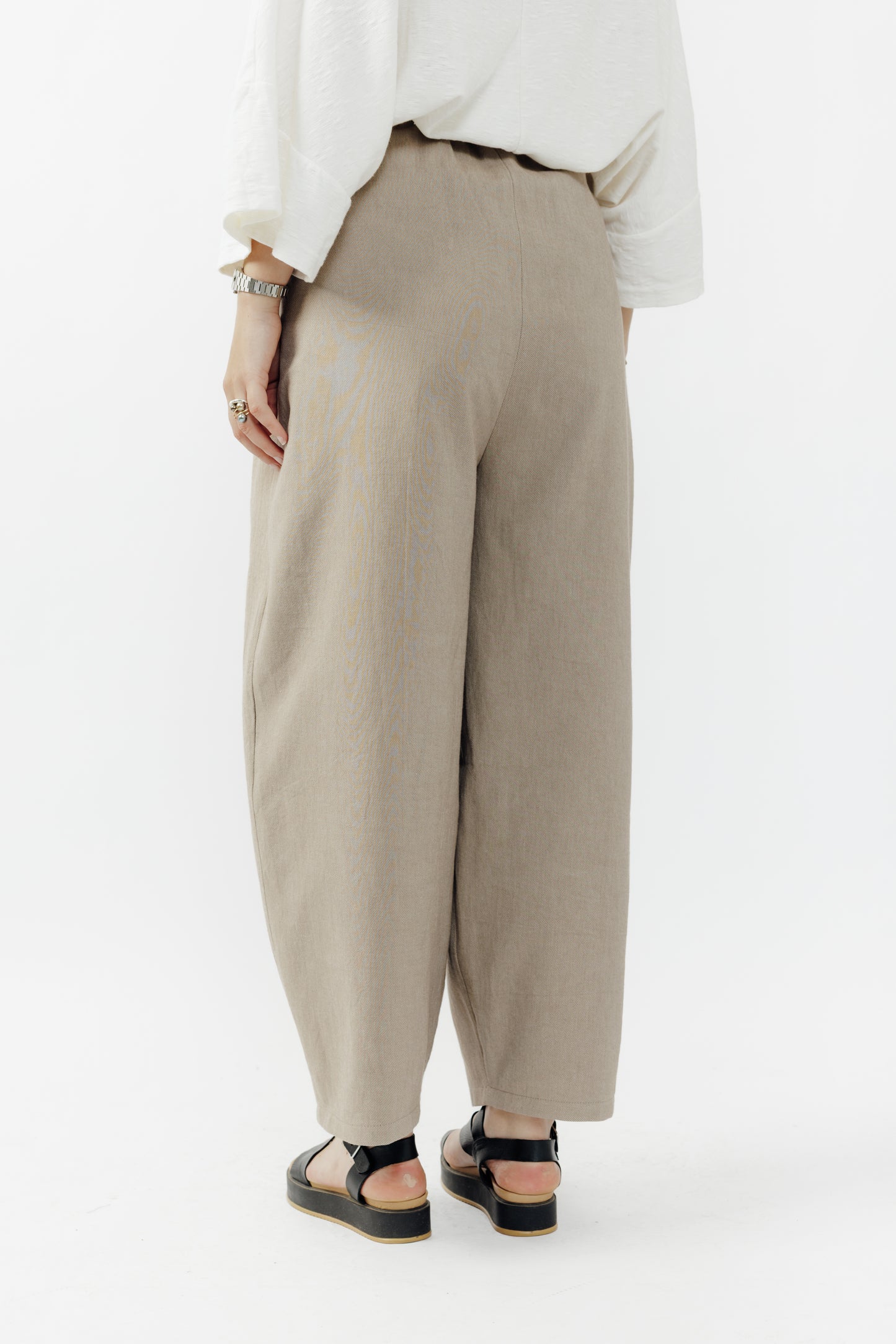 Pantalon circulaire de la marque Aïdama, coupe ballon en coton marron glacé avec ceinture ajustable. Porté par une mannequin femme et vu de dos.