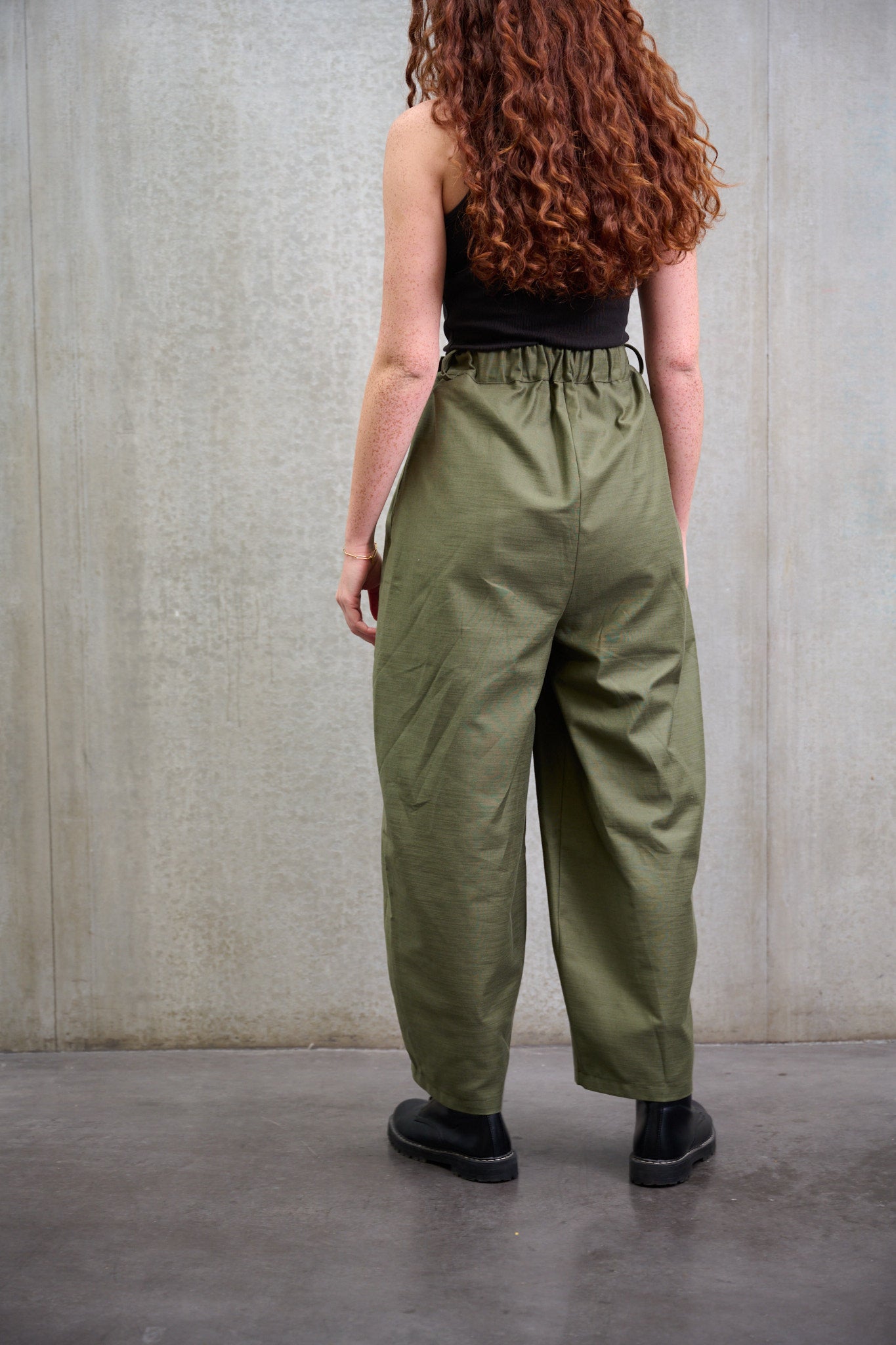 Pantalon circulaire Aïdama, coupe ballon avec ceinture ajustable en coton texturé vert. Porté par une mannequin femme et vu de dos.