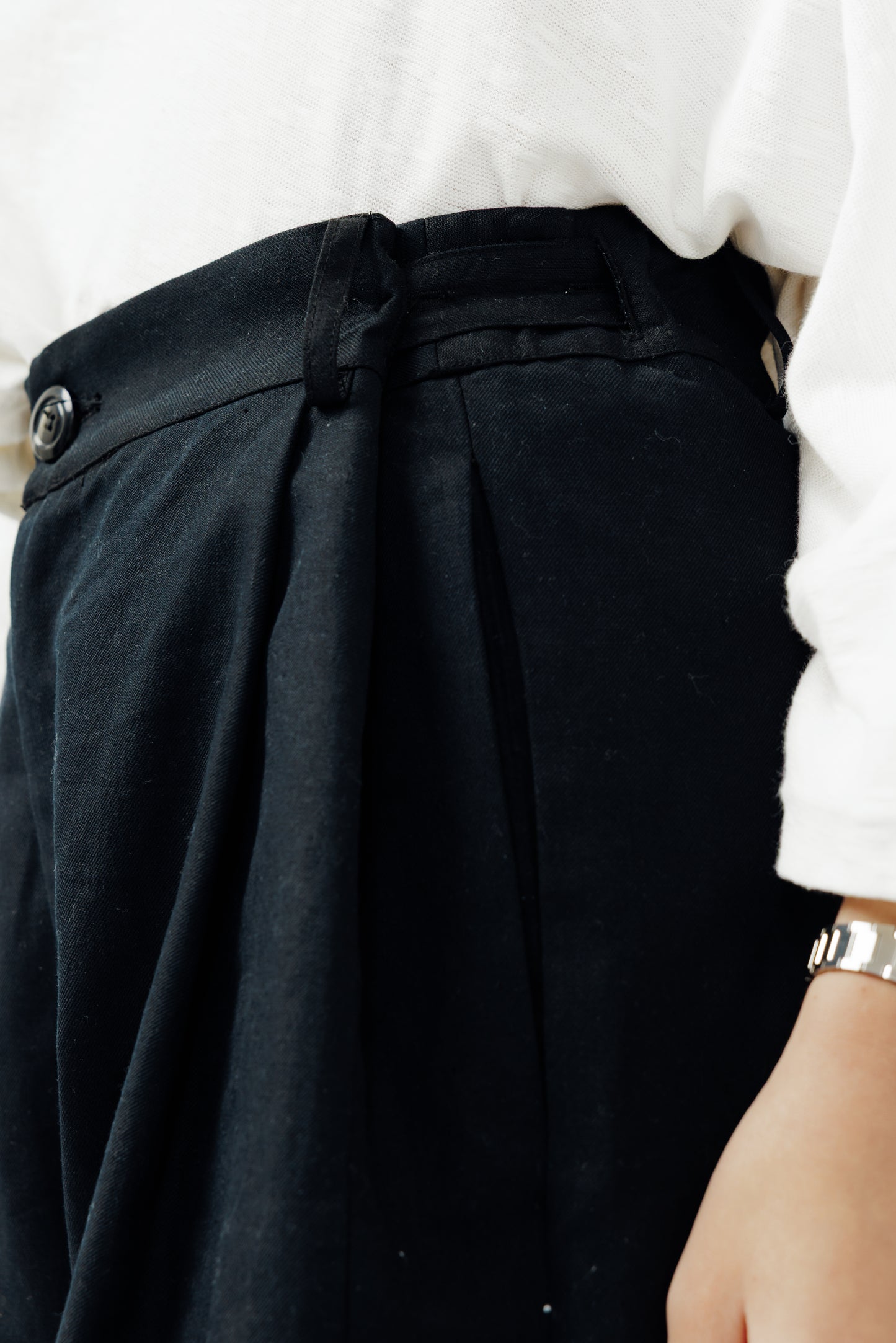 Pantalon droit de la marque Aïdama, coupe ample en coton et lin noir avec sangles ajustables à la taille. Porté par une mannequin femme et vu de profil zoomé sur la ceinture.
