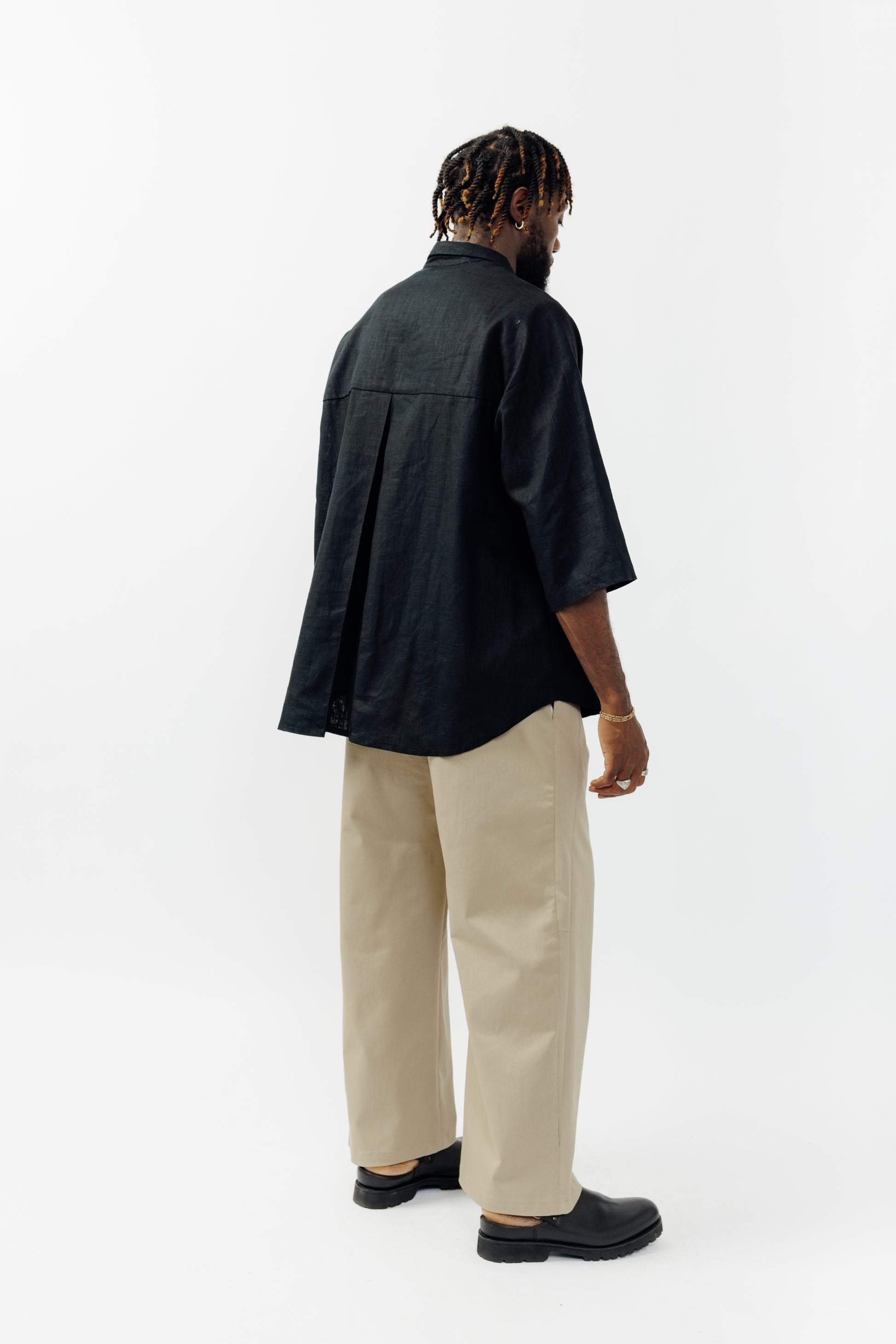 Pantalon droit de la marque Aïdama, coupe ample en gabardine de coton beige avec sangles ajustables à la taille. Porté par un mannequin homme et vu de dos.