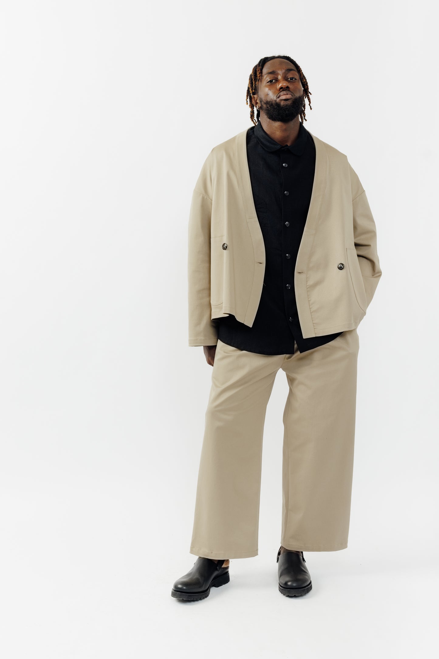 Pantalon droit de la marque Aïdama, coupe ample en gabardine de coton beige avec sangles ajustables à la taille. Porté par un mannequin homme et vu de face.