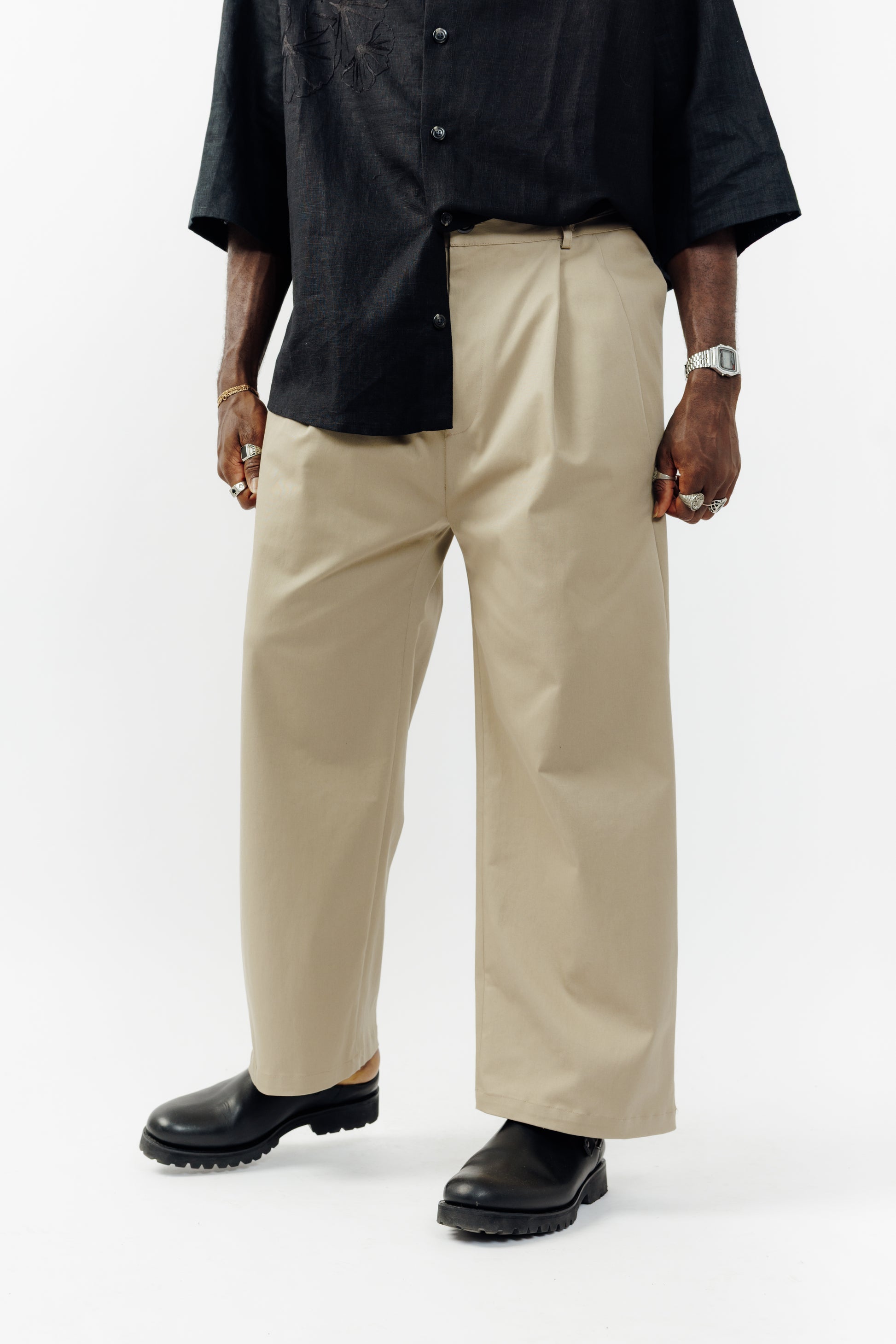 Pantalon droit de la marque Aïdama, coupe ample en gabardine de coton beige avec sangles ajustables à la taille. Porté par un mannequin homme et vu de face zoomé sur les jambes.