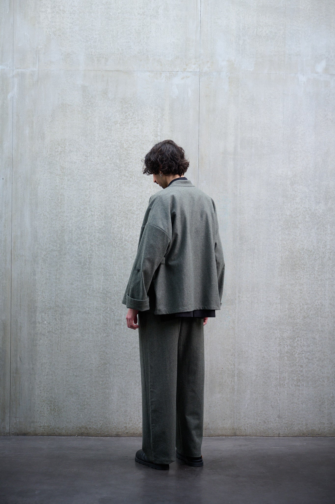 Pantalon droit de la marque Aïdama, coupe large en flanelle de laine grise. Porté par un mannequin homme et vue de dos.