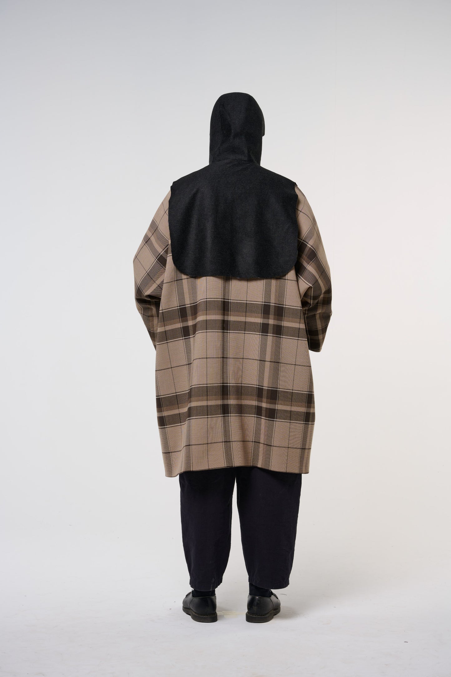 Plastron à capuche de la marque Aïdama, modèle Do en laine noire. Porté capuche relevée, par un mannequin homme et vu de dos.