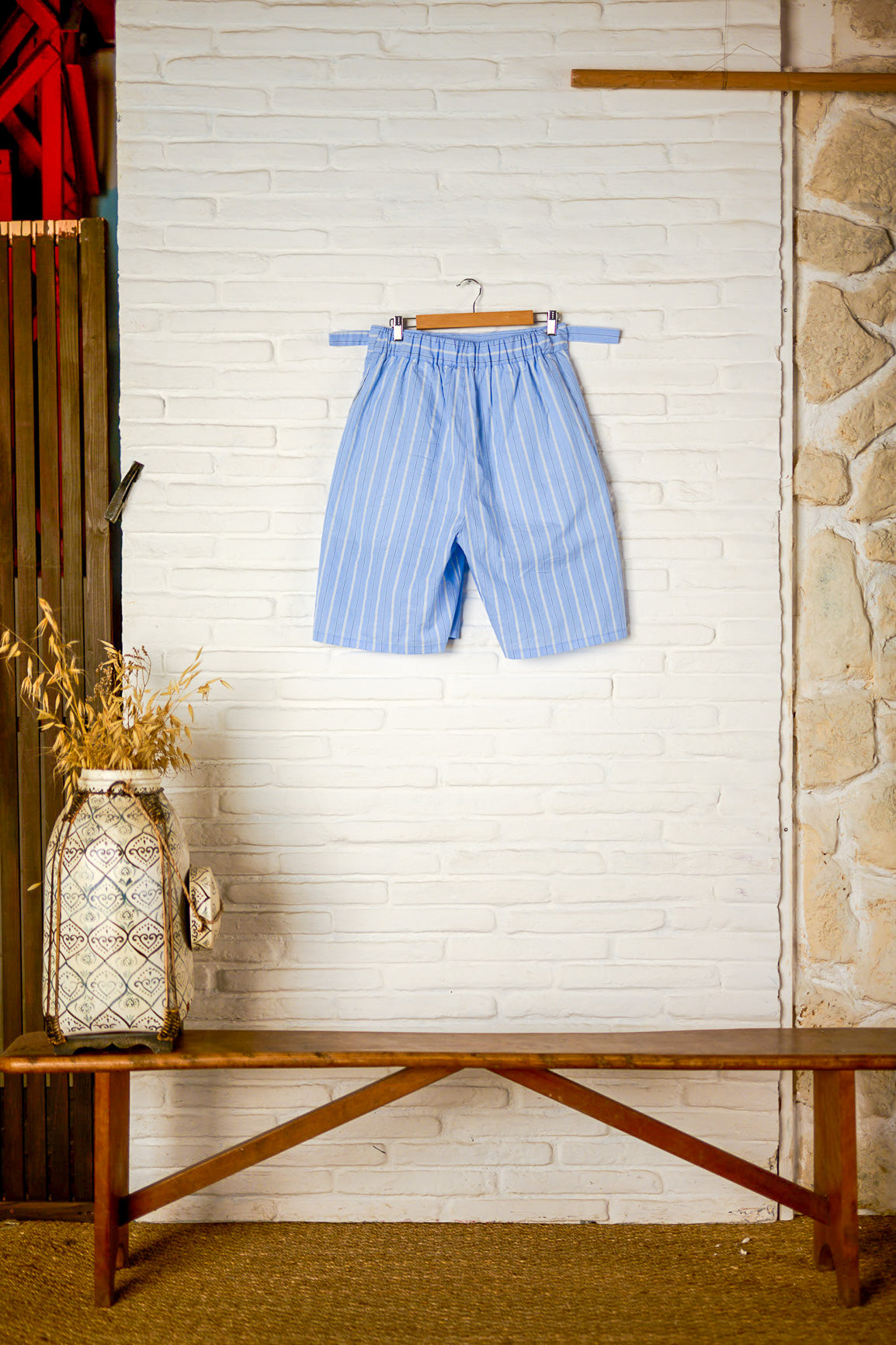 Short ballon de la marque Aïdama en coton bleu à rayures avec ceinture ajustable. Vu sur ceintre de dos.