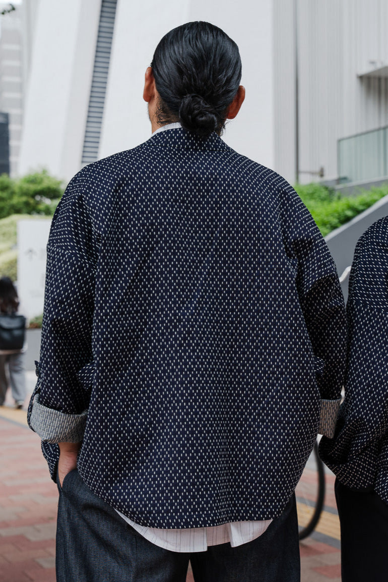Veste croisée à col kimono de la marque Aïdama, modèle Samue en coton japonais bleu brodé de points Sashiko. Portée par un mannequin homme et vue de dos.
