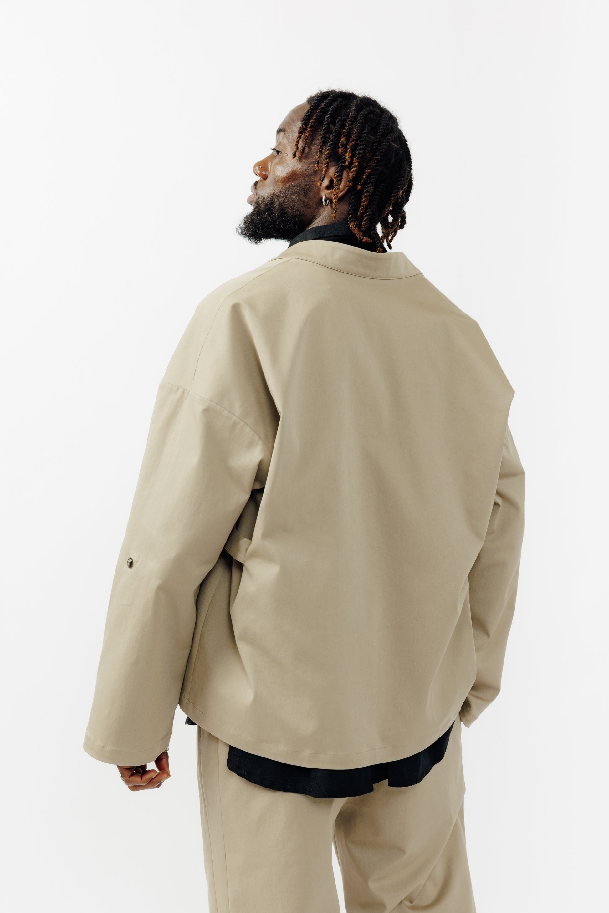 Veste croisée à col kimono de la marque Aïdama, modèle samue en gabardine de coton beige. Portée ouverte par un mannequin homme et vu de dos.